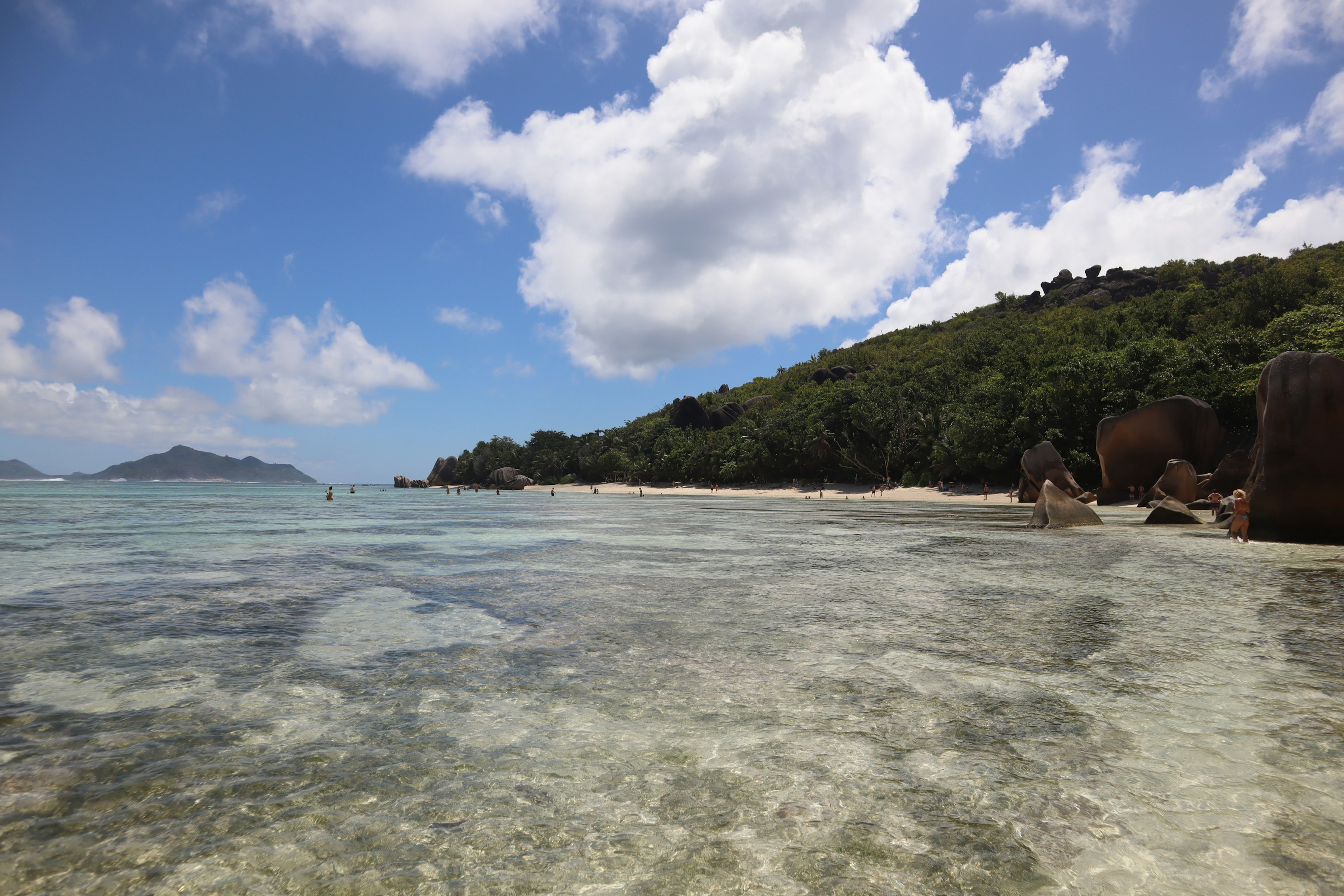 Clear turquoise water under a blue sky with white clouds and lush green hills