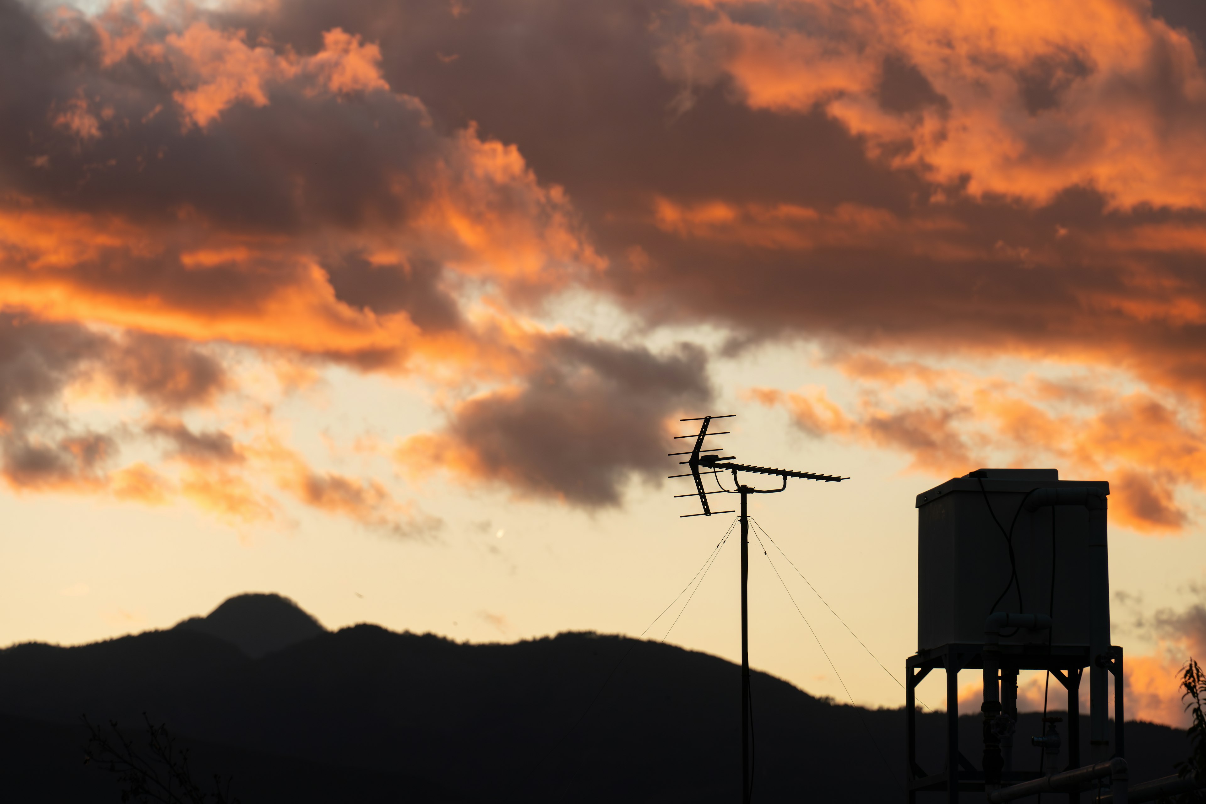 Silueta de montañas y tanque de agua contra un vibrante atardecer