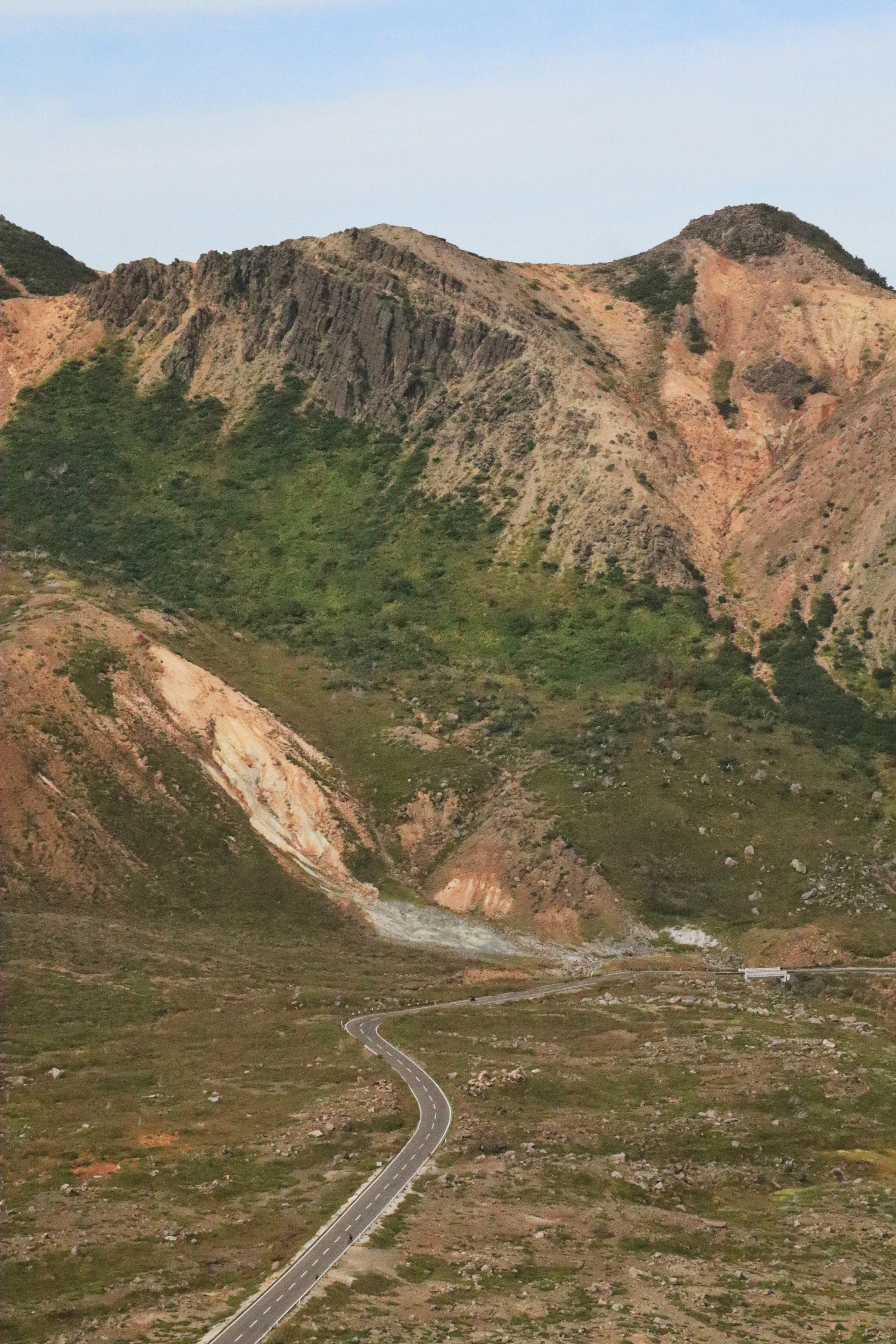 Winding road through green grassland with mountainous background