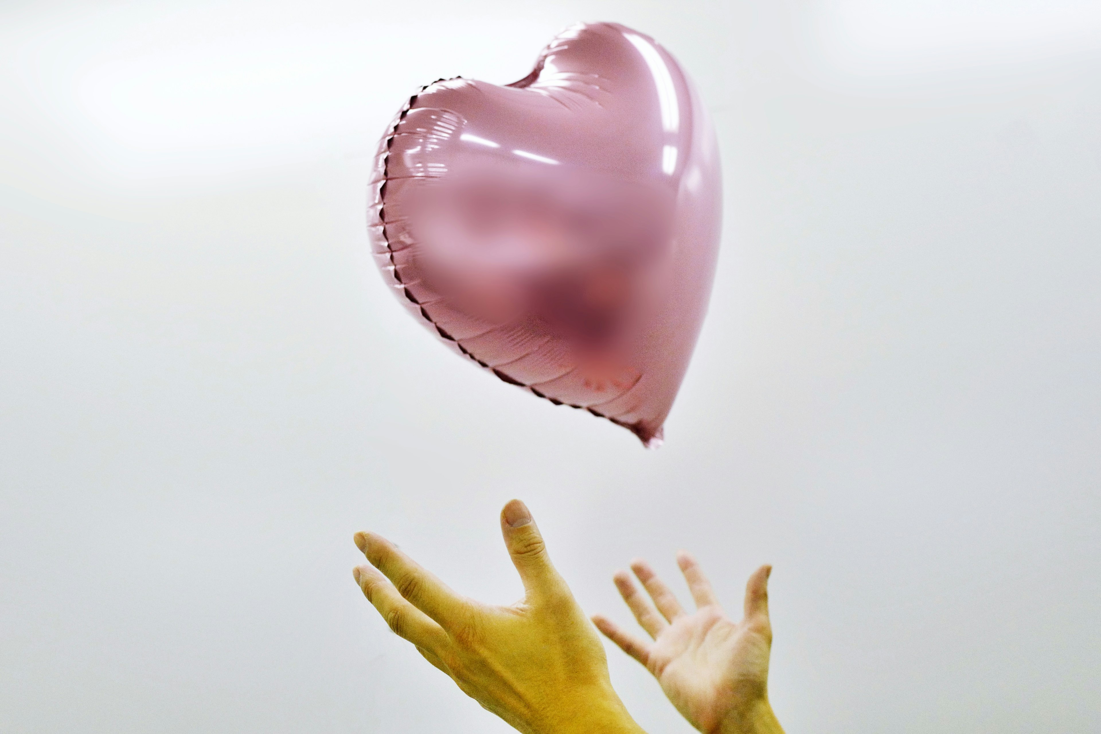 A pink heart-shaped balloon floating above hands