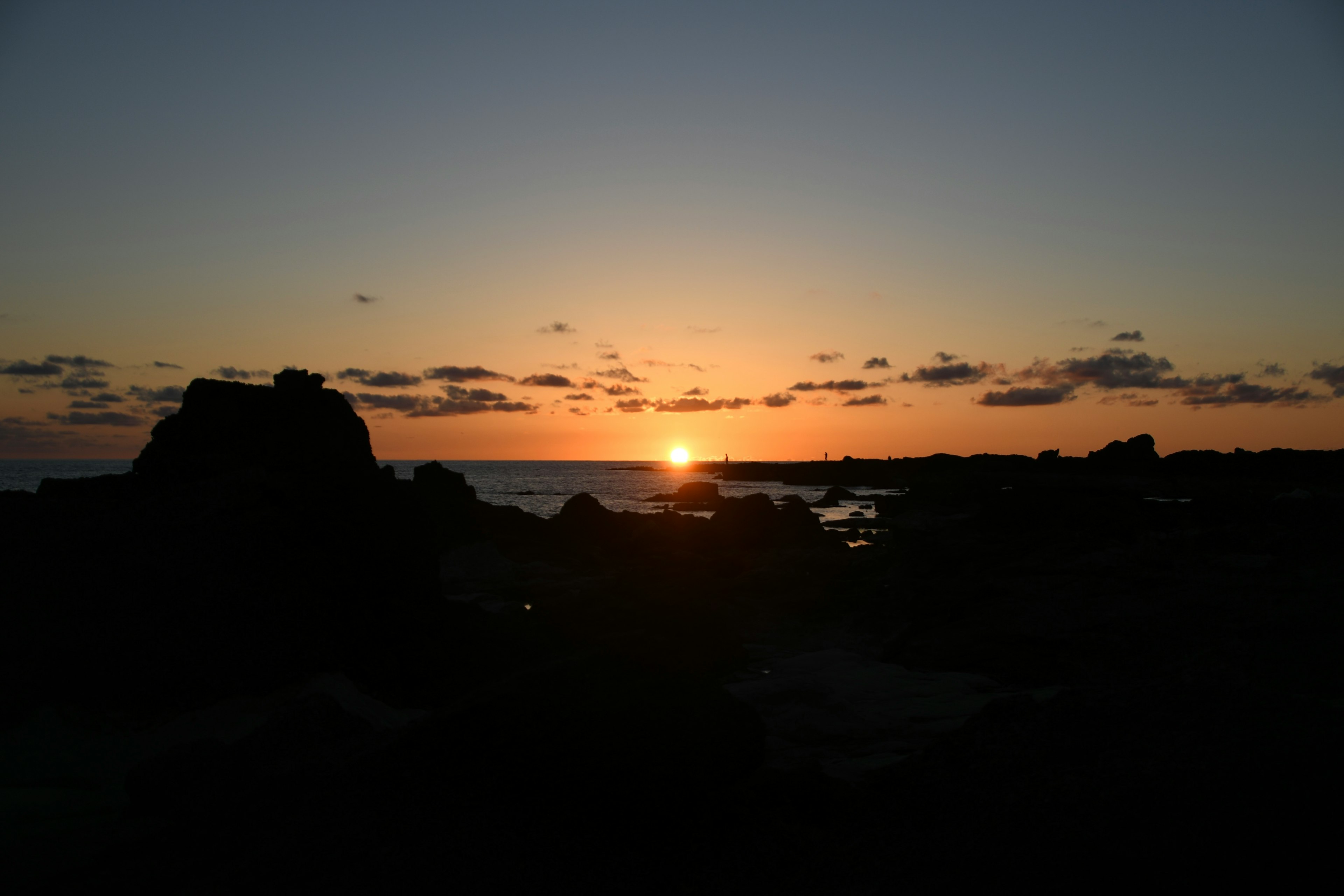 Silhouette di rocce contro un'alba sull'oceano