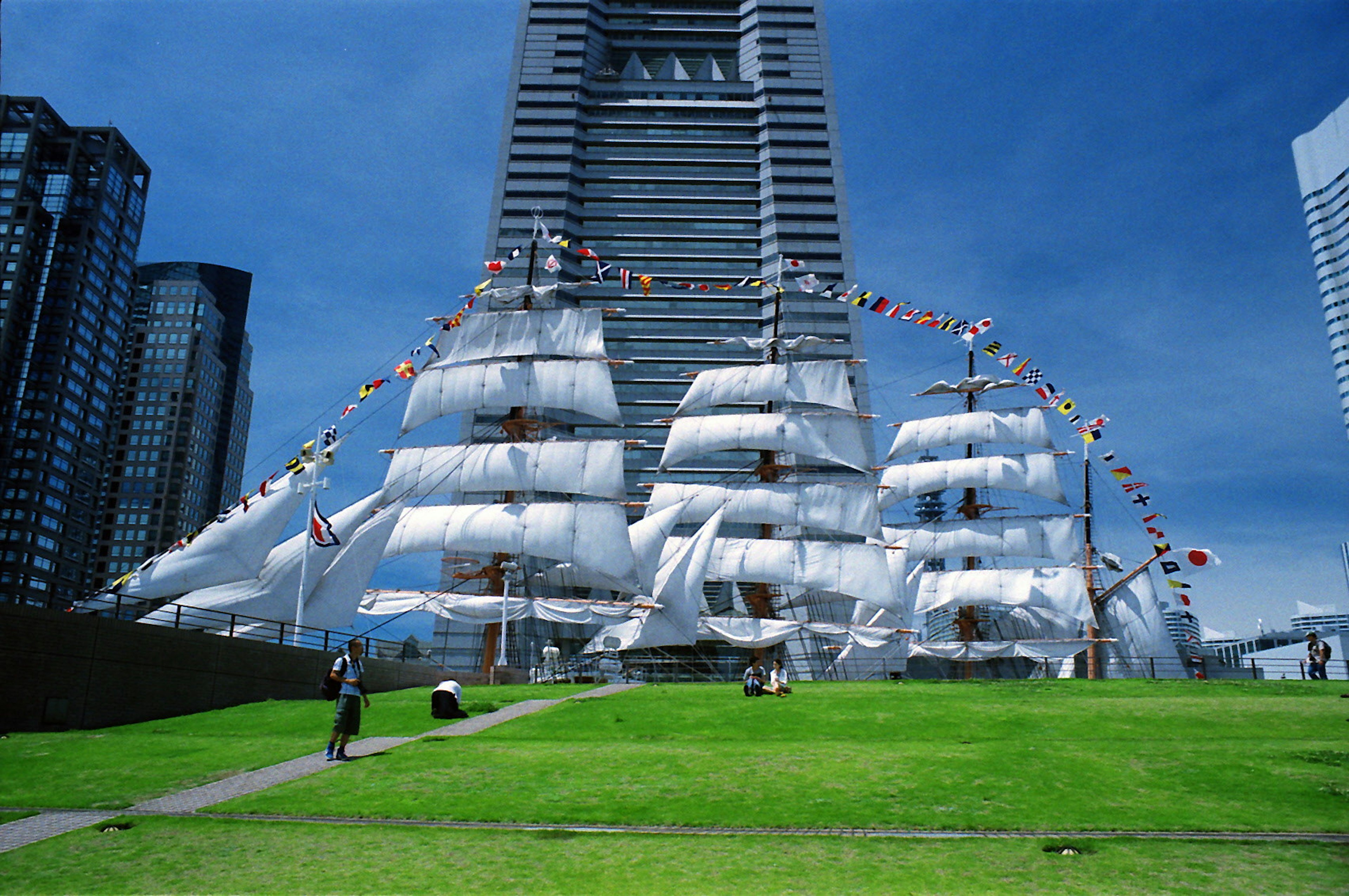 Exhibition of sailing ships in front of a skyscraper with blue sky and green grass