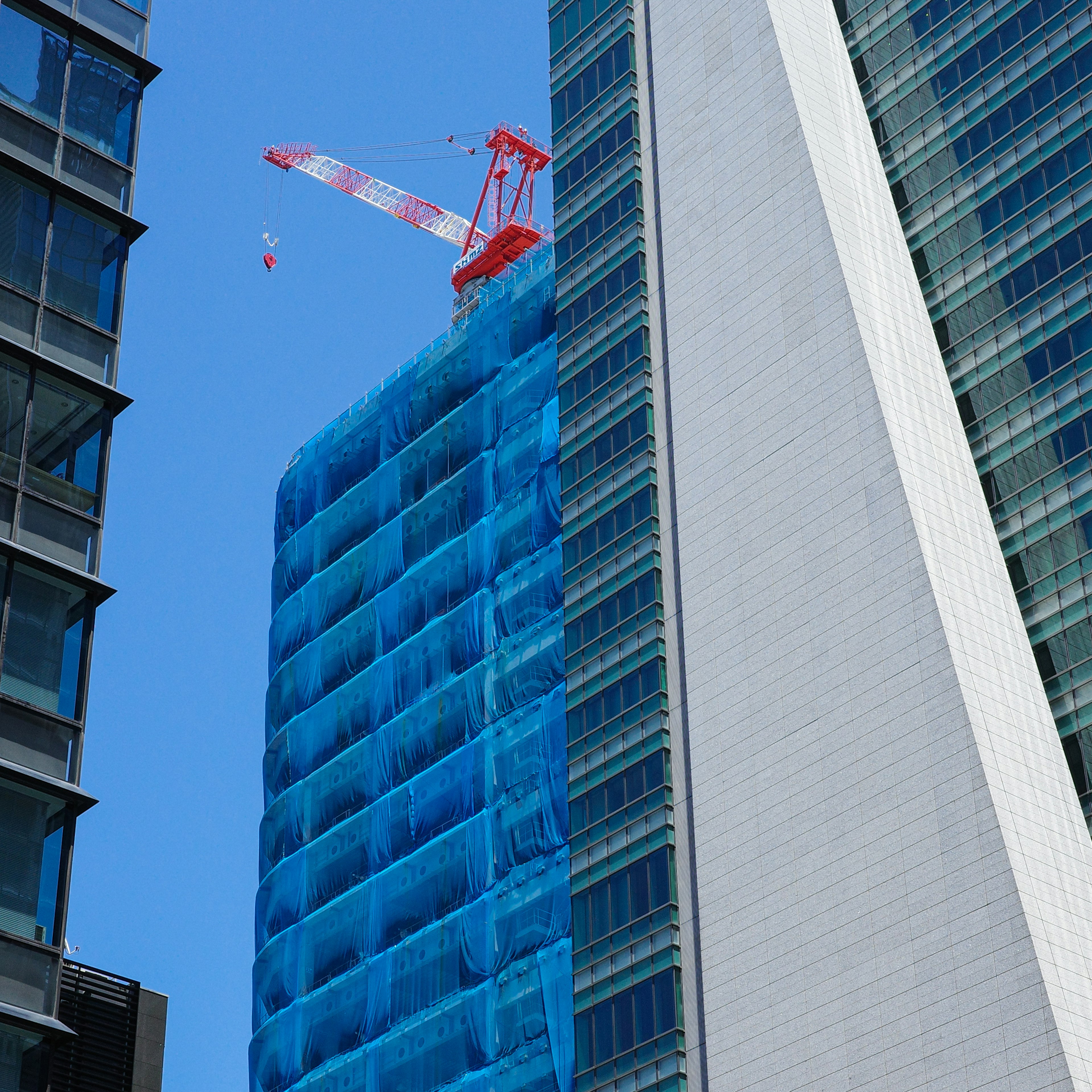 Baustelle eines Hochhauses, das mit blauem Netz bedeckt ist, mit umliegenden Wolkenkratzern