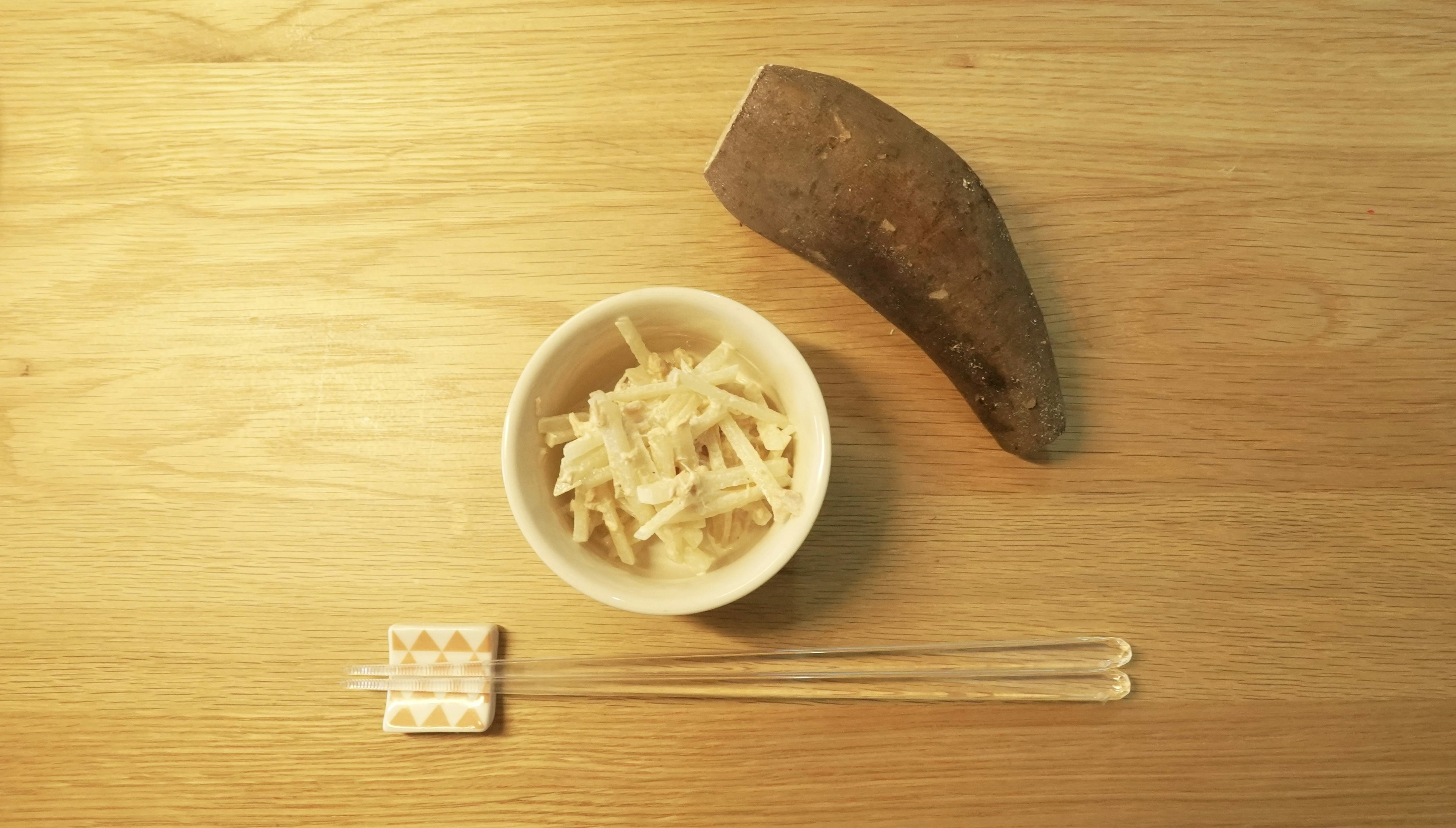 Un bol blanc avec des légumes râpés sur une table en bois à côté d'une grande patate douce