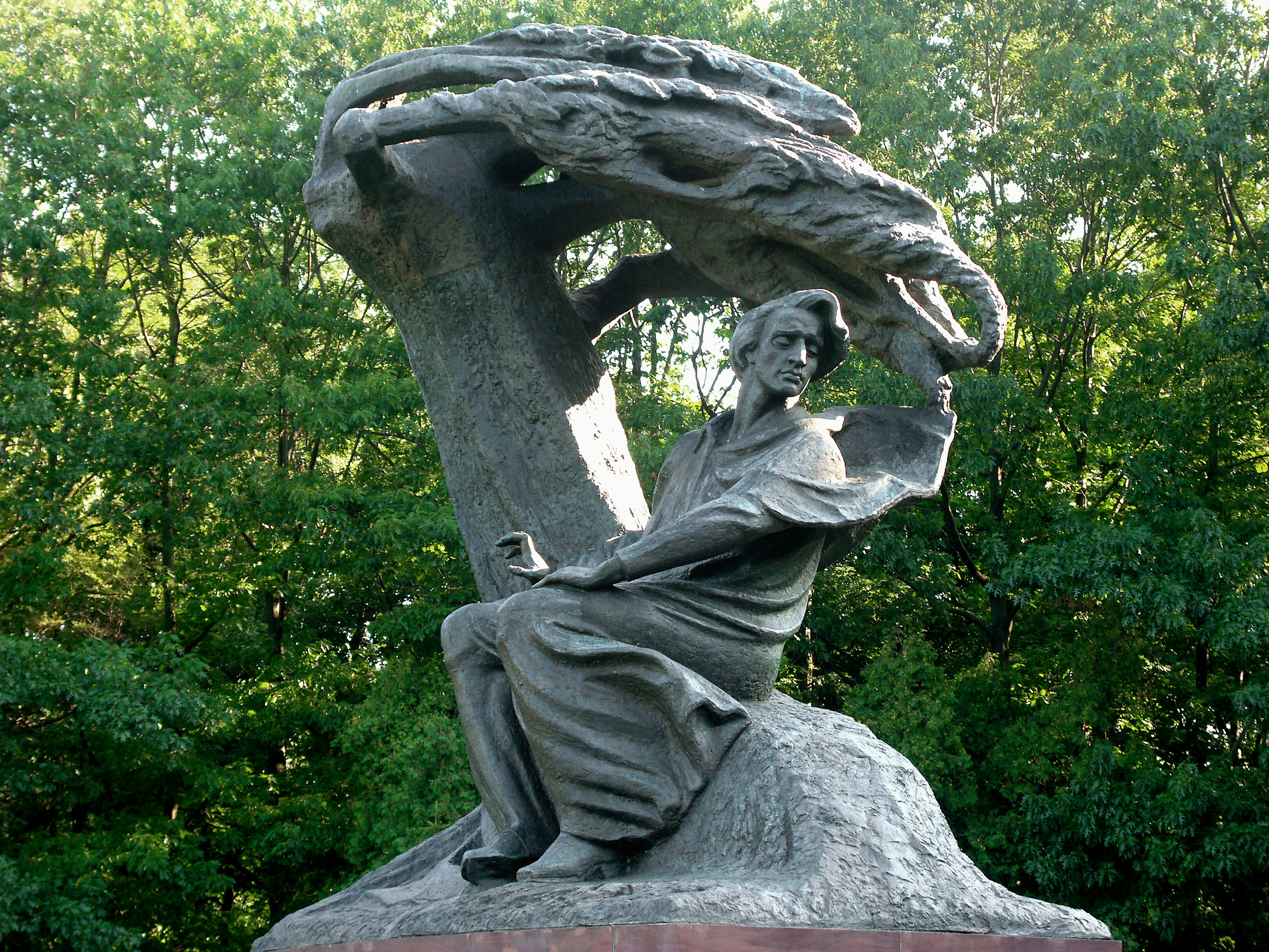 Sculpture of a seated figure under a tree with an eagle above