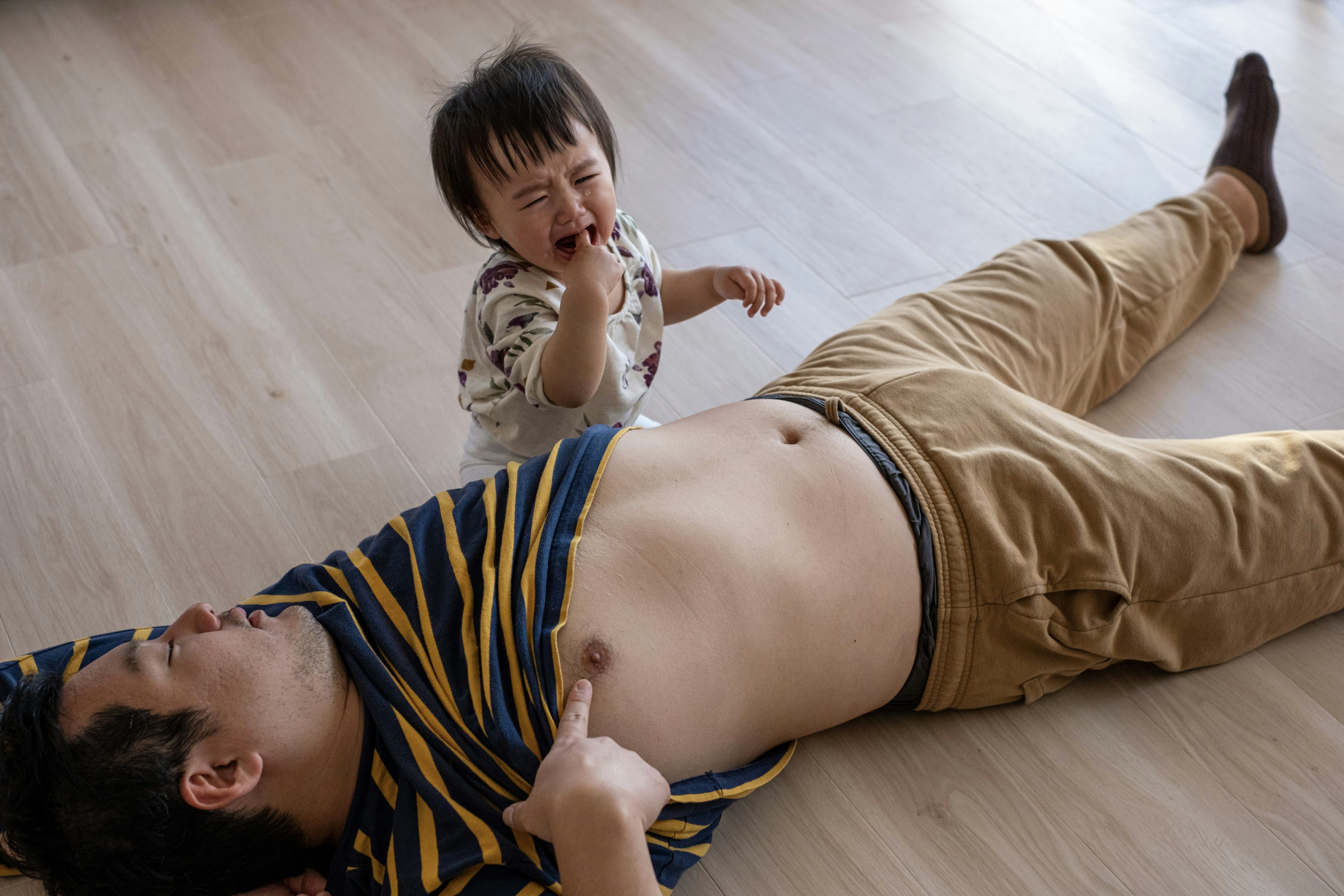 Un padre acostado en el suelo con un niño que juega y llora