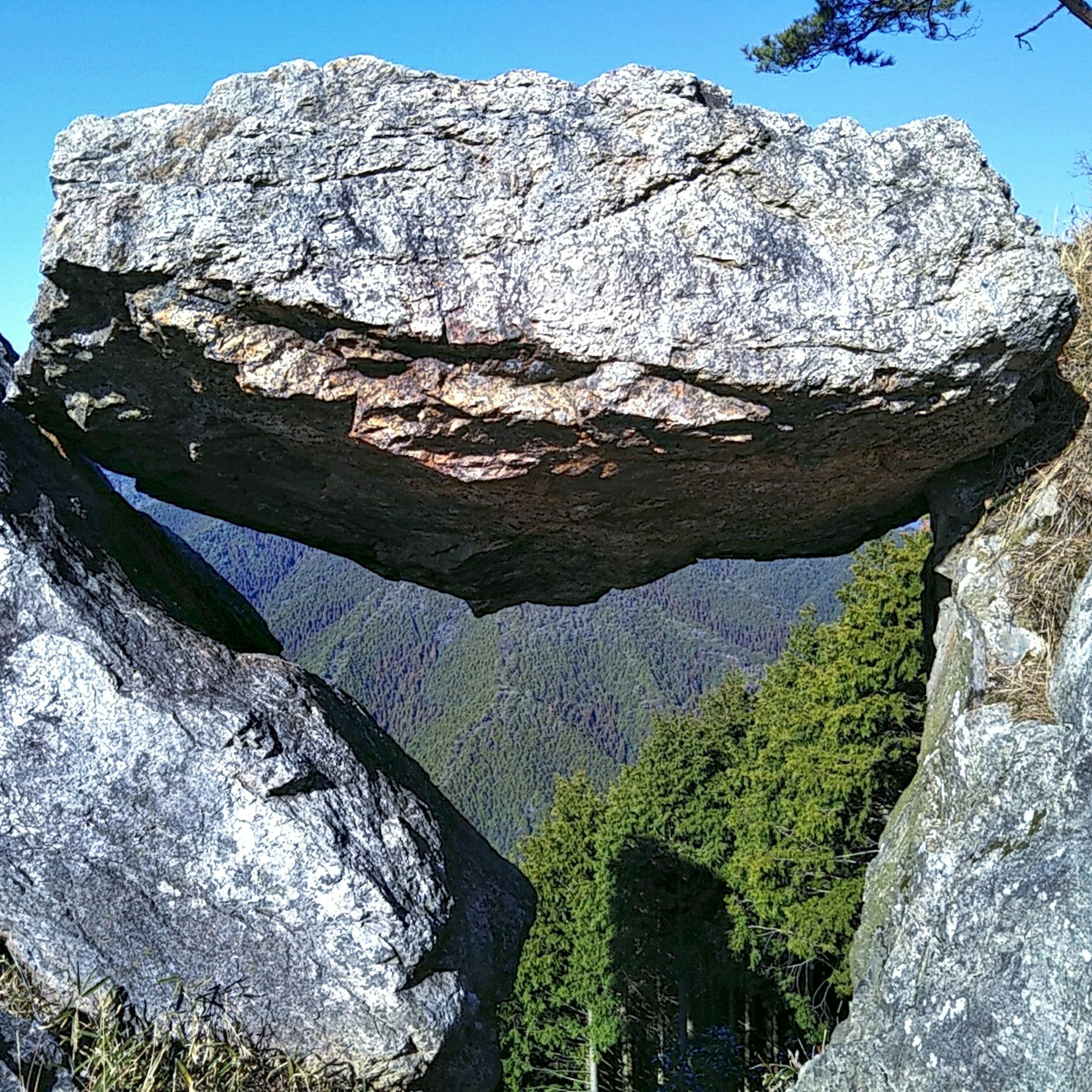 两块岩石之间平衡的大岩石，背景是绿色的山脉