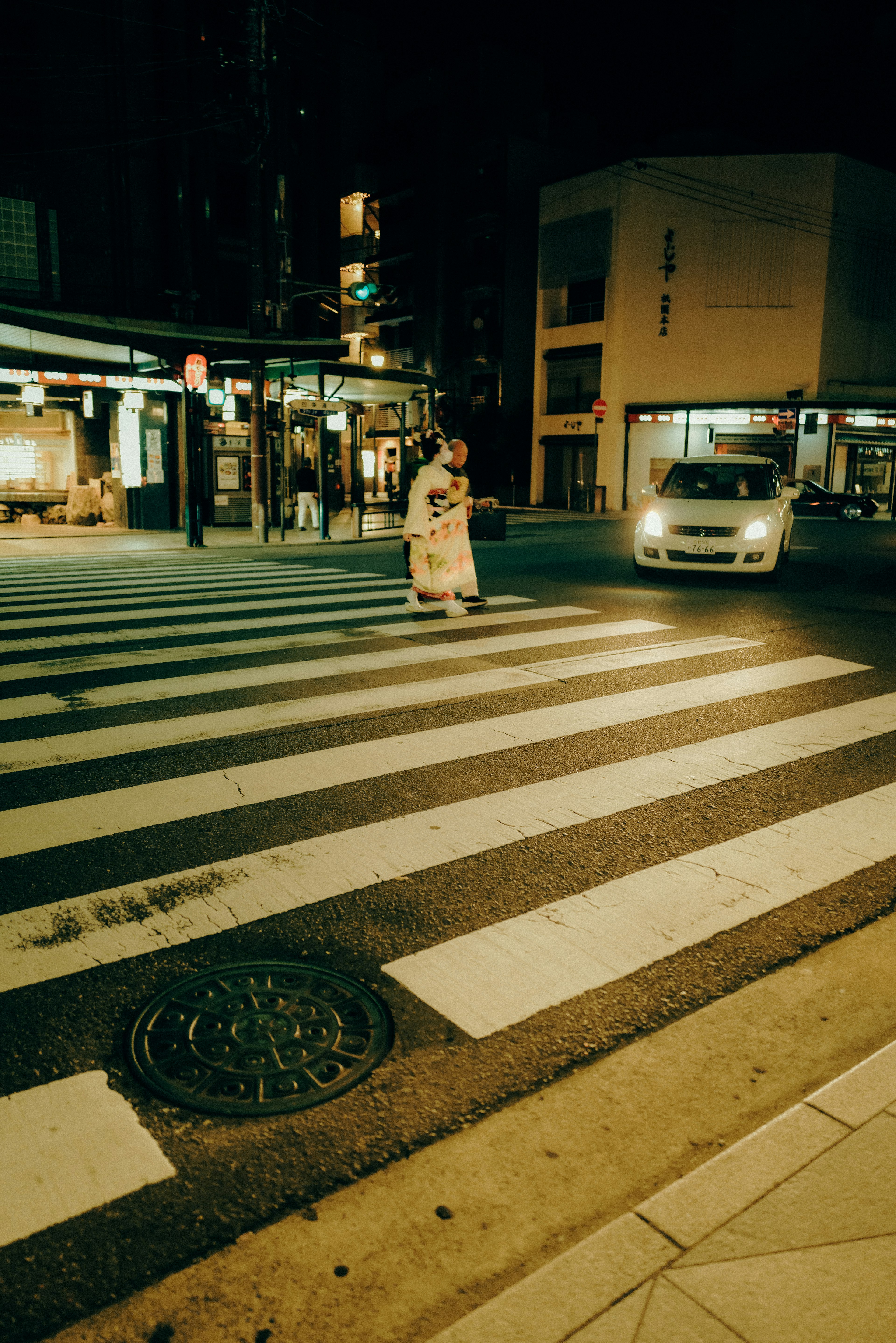 A person crossing the street at night with a car approaching