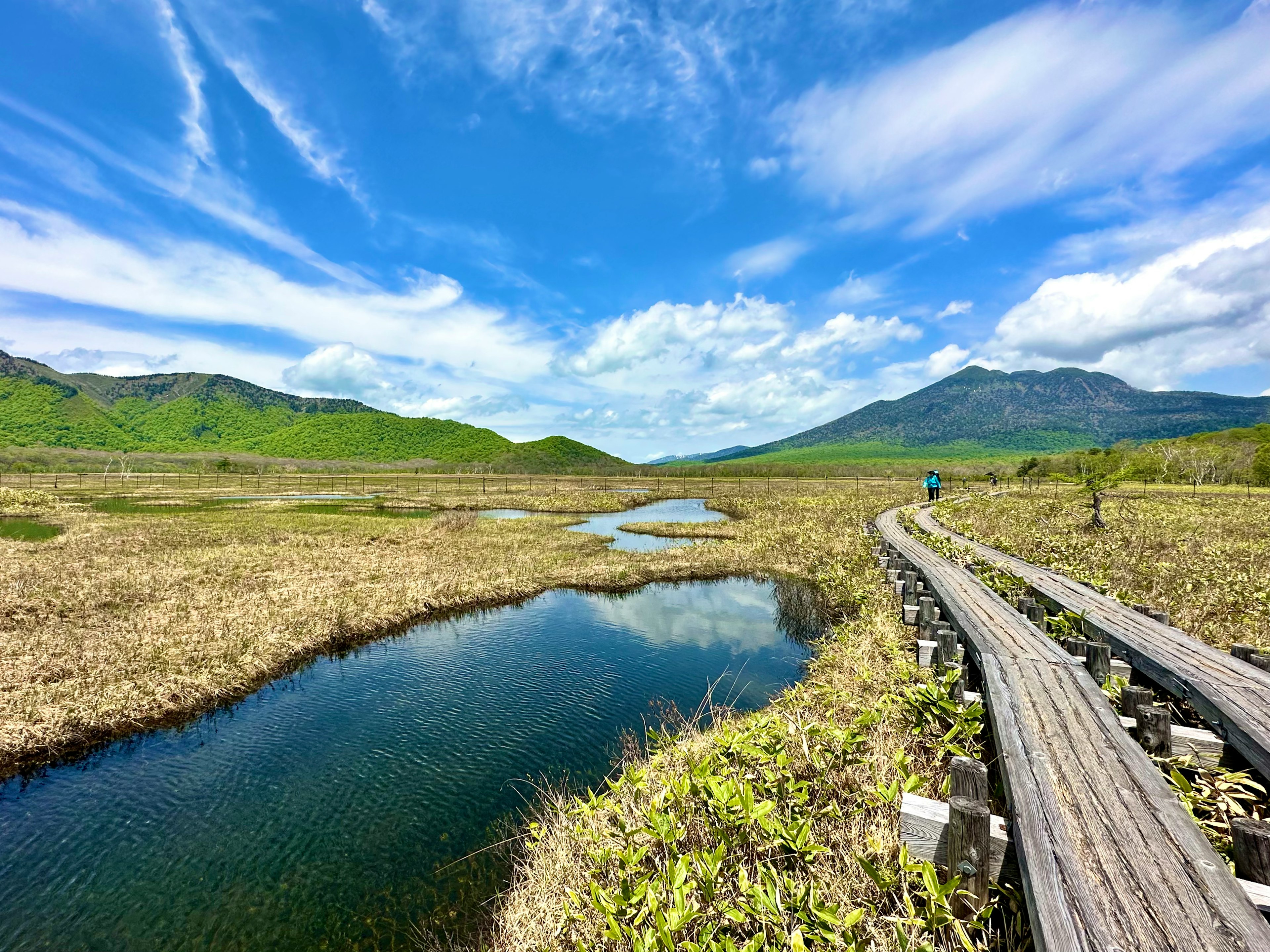 Wooden walkway in a wetland surrounded by green mountains and blue sky