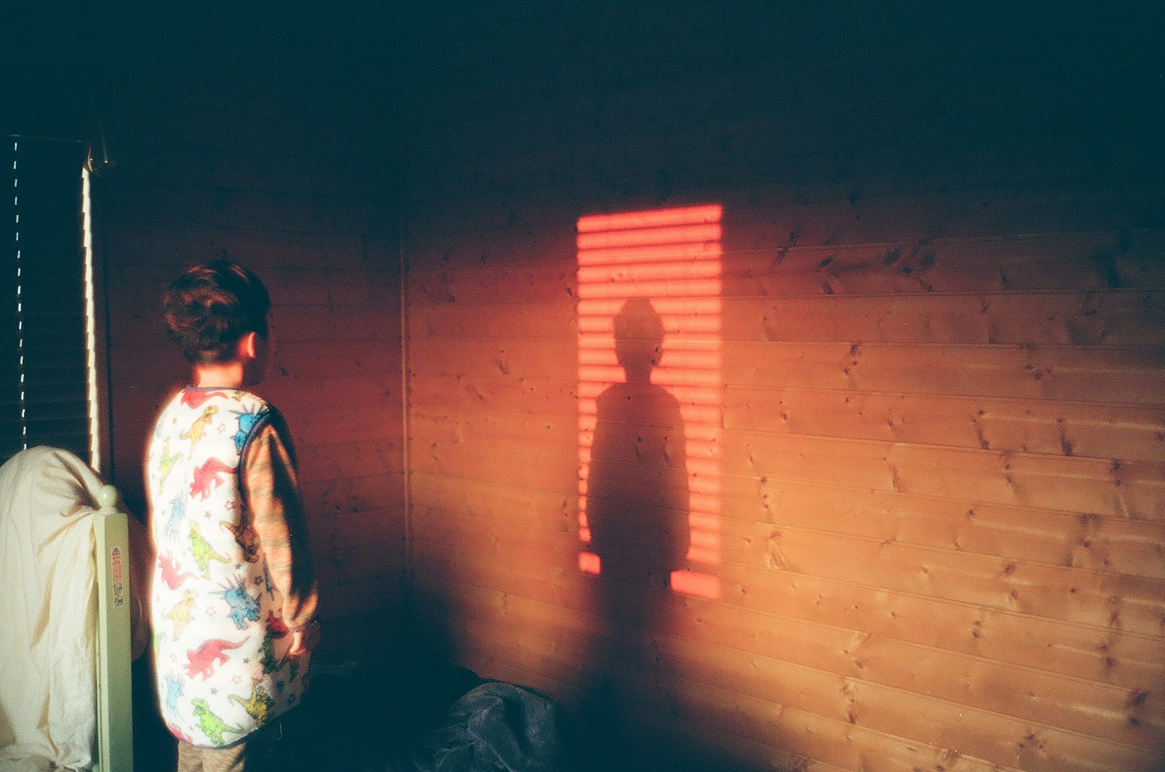 Kind steht vor Fensterjalousien und wirft einen roten Schatten an die Wand
