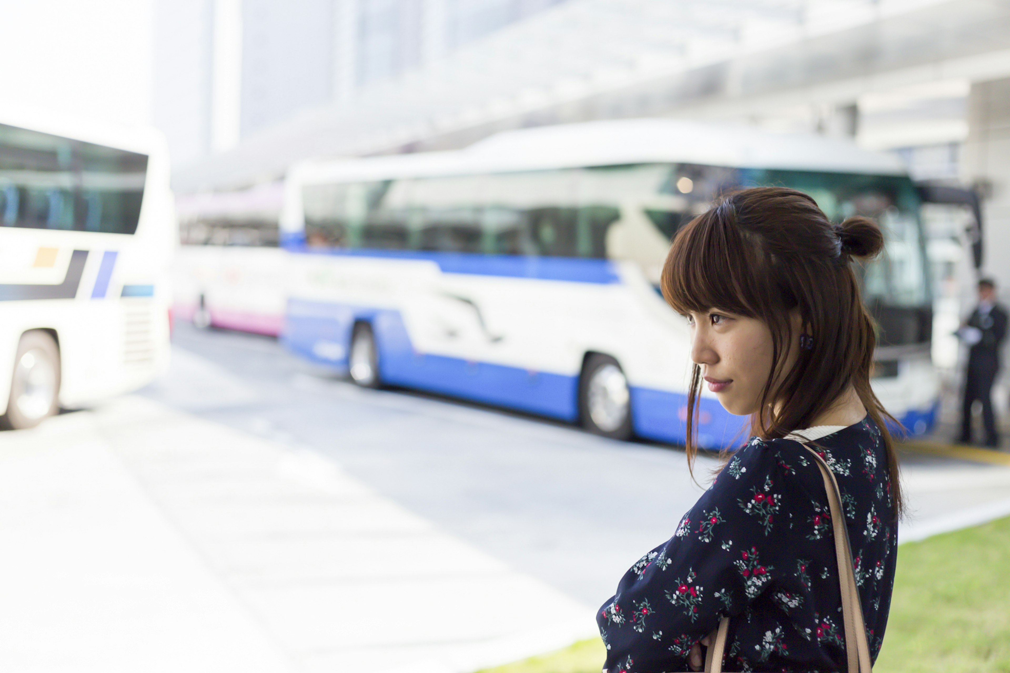 Perfil de una mujer esperando en una parada de autobús con autobuses al fondo