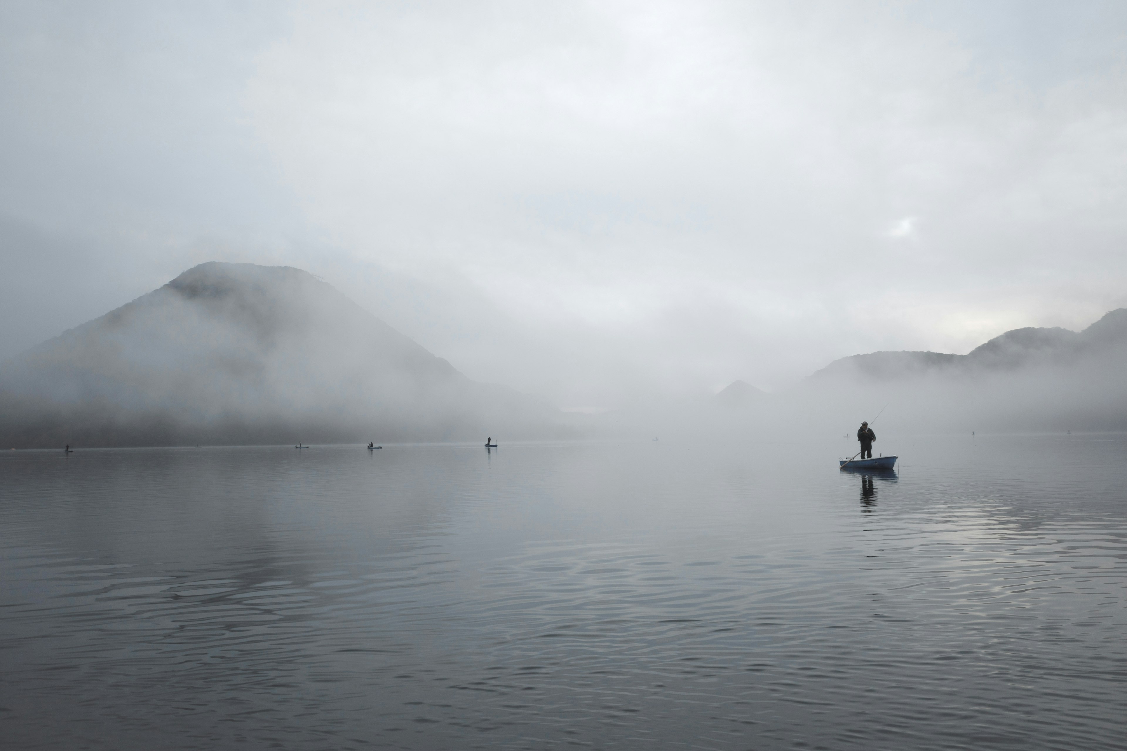 A person in a small boat on a calm lake shrouded in fog