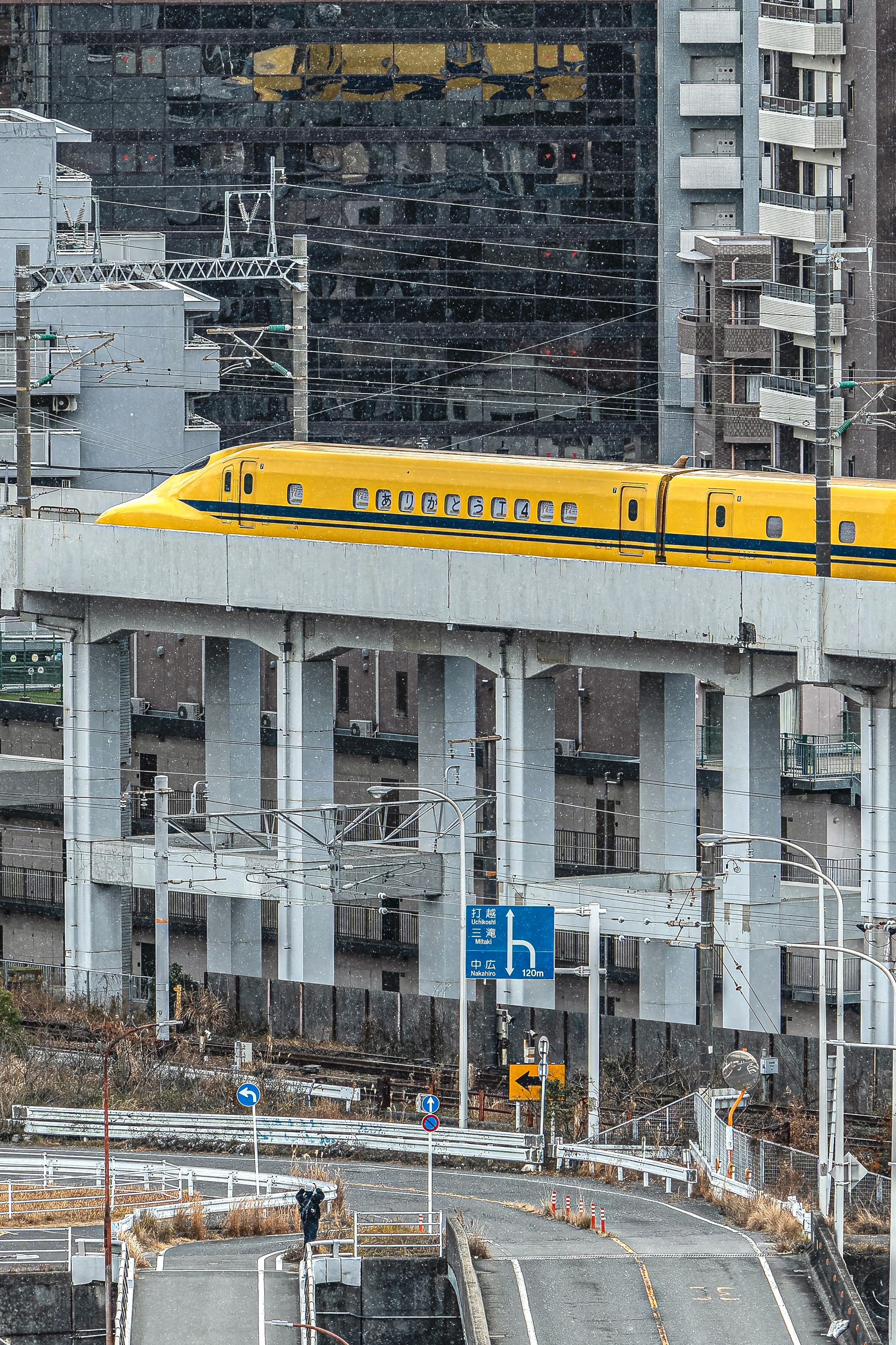 Train Shinkansen jaune sur une voie élevée dans un environnement urbain