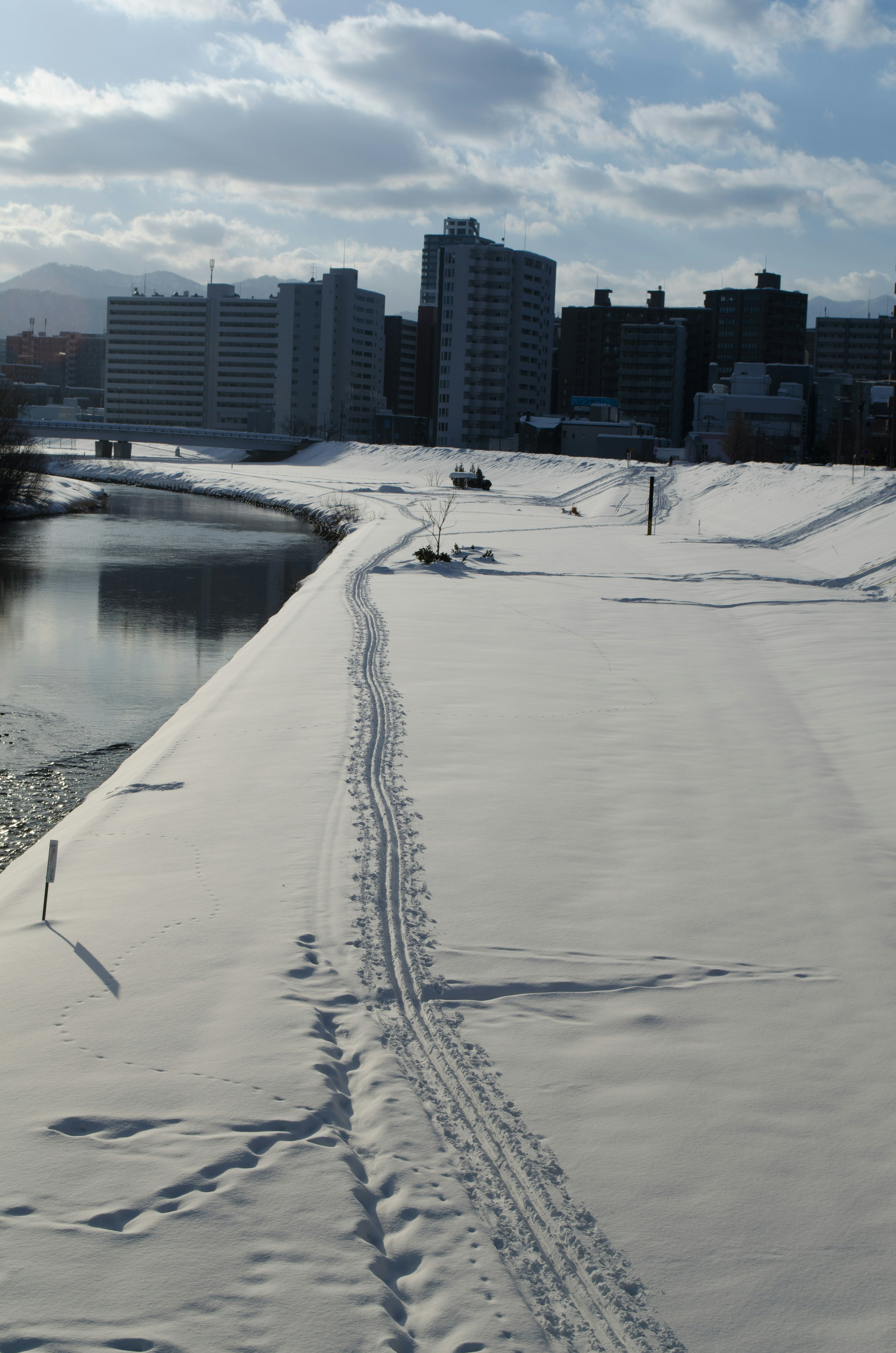 Schneebedeckter Flussufer mit Gebäuden im Hintergrund