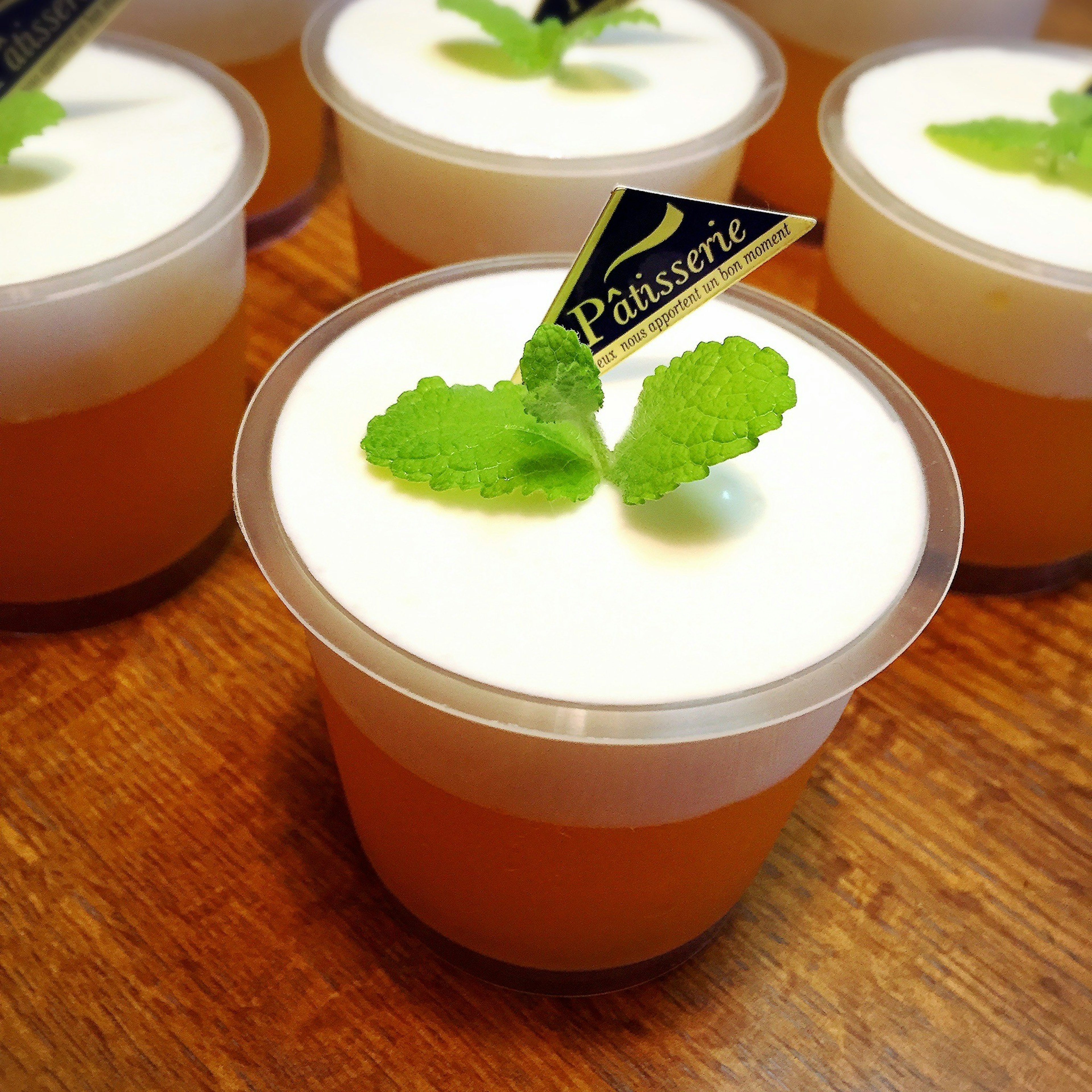 Set of dessert cups with cream and mint leaves on top featuring a patisserie logo