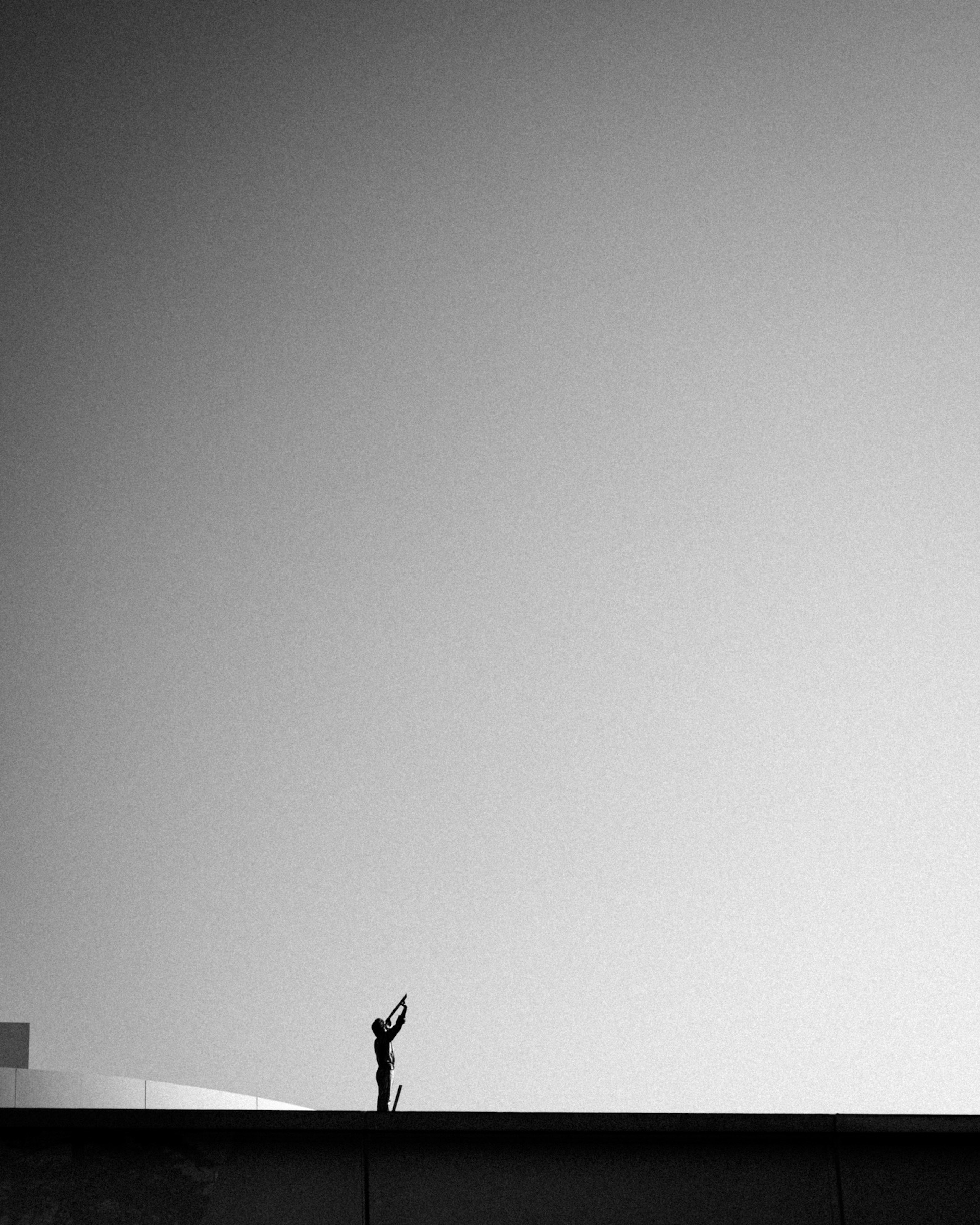 Una figura de pie en un borde alcanzando el cielo en un paisaje en blanco y negro