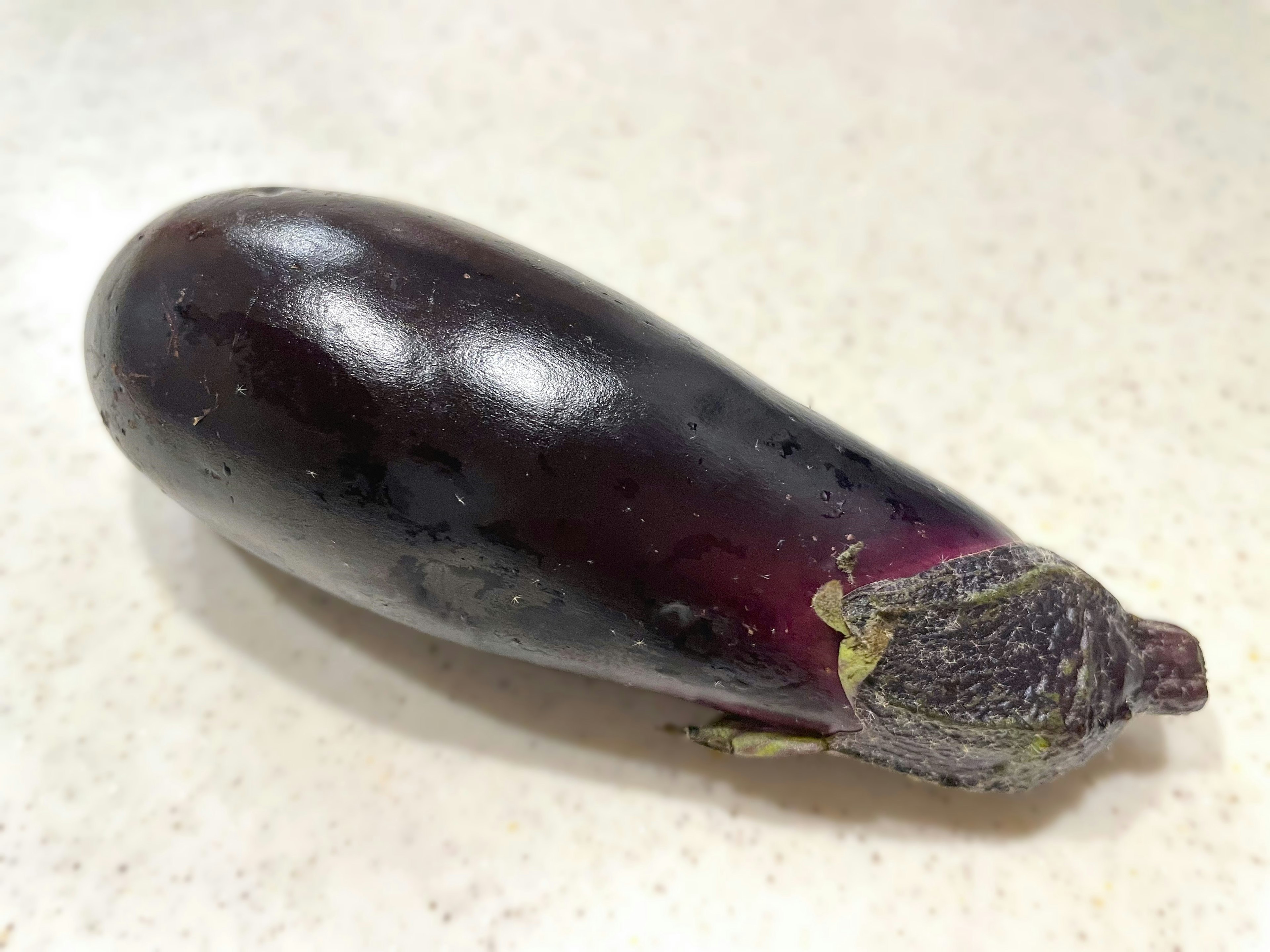 Eine lila Aubergine liegt auf einer weißen Arbeitsplatte