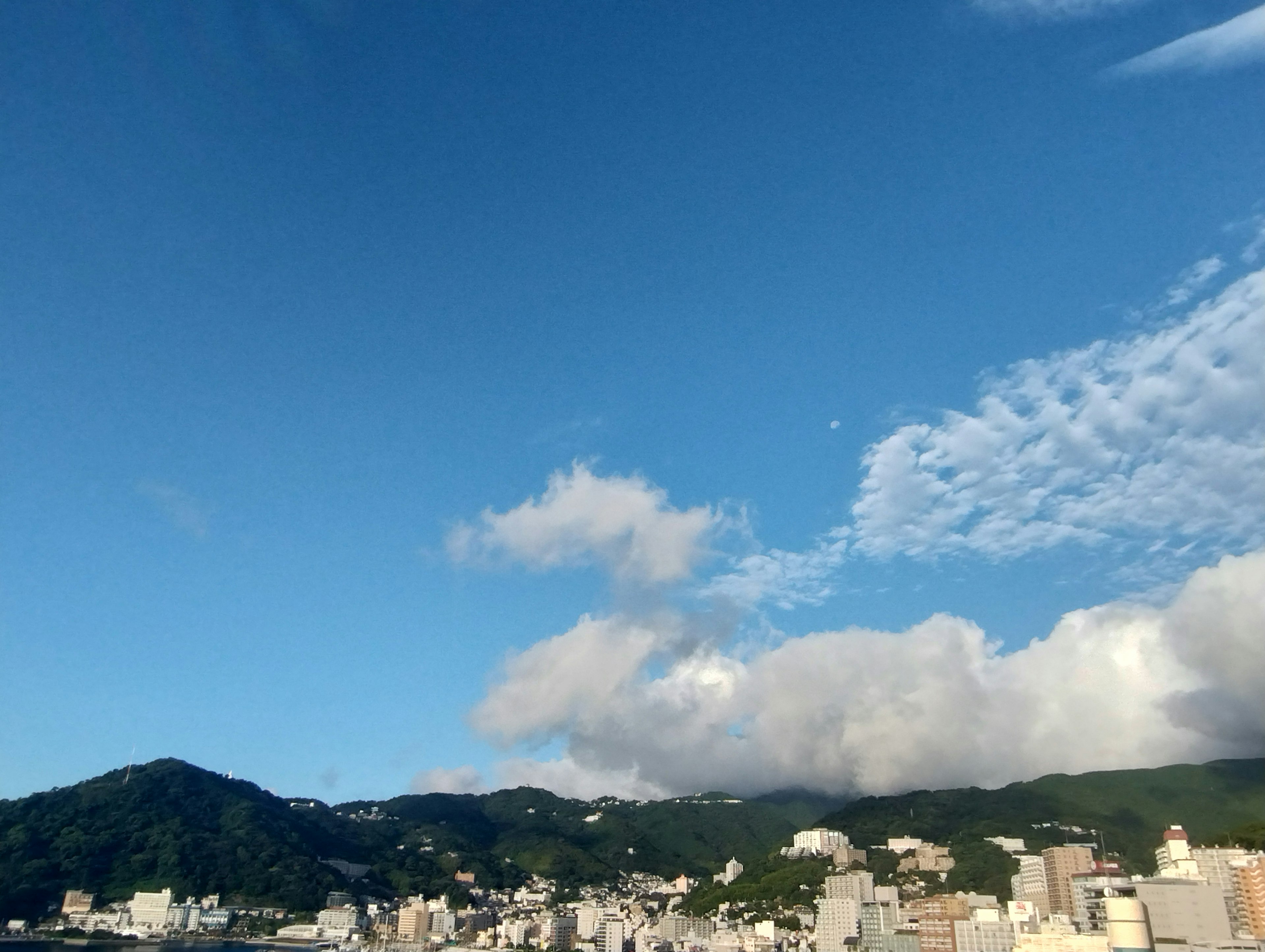 Vista panoramica di un cielo blu con nuvole e un paesaggio montuoso che sovrasta una città