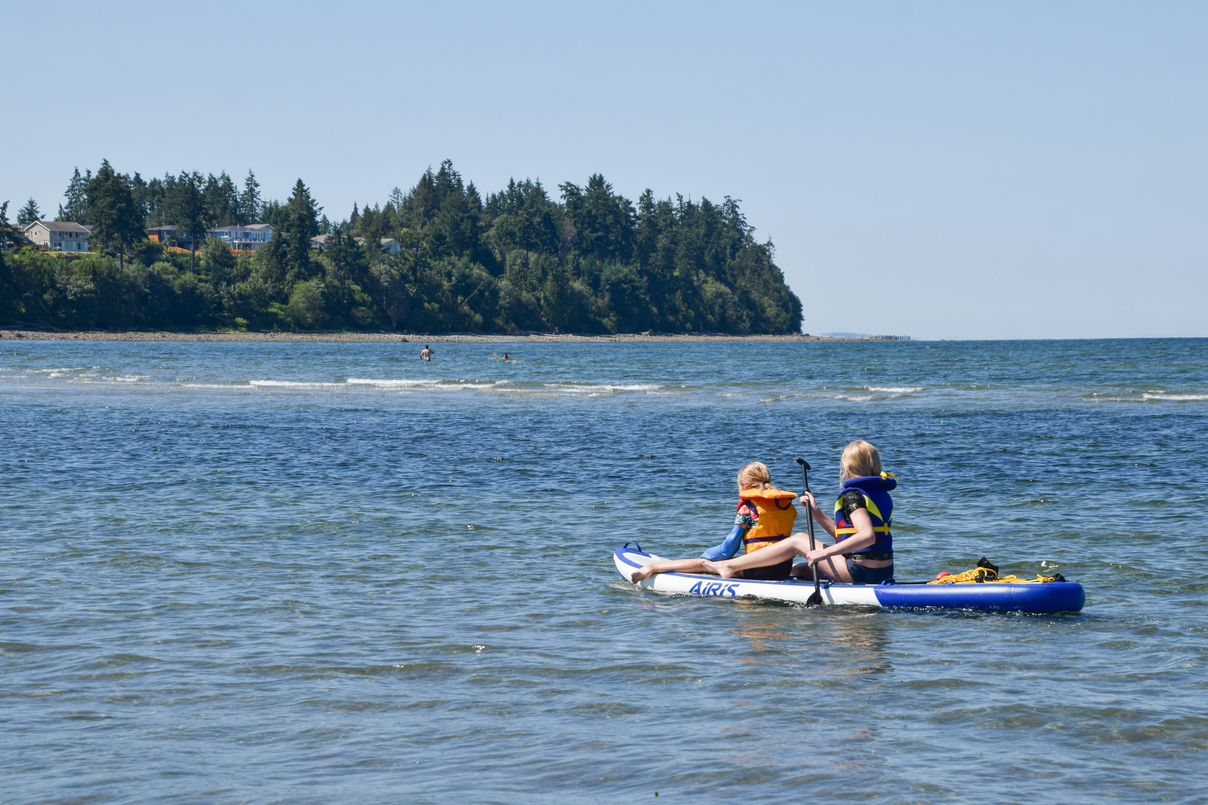 Two children kayaking on a calm sea with a lush green island in the background