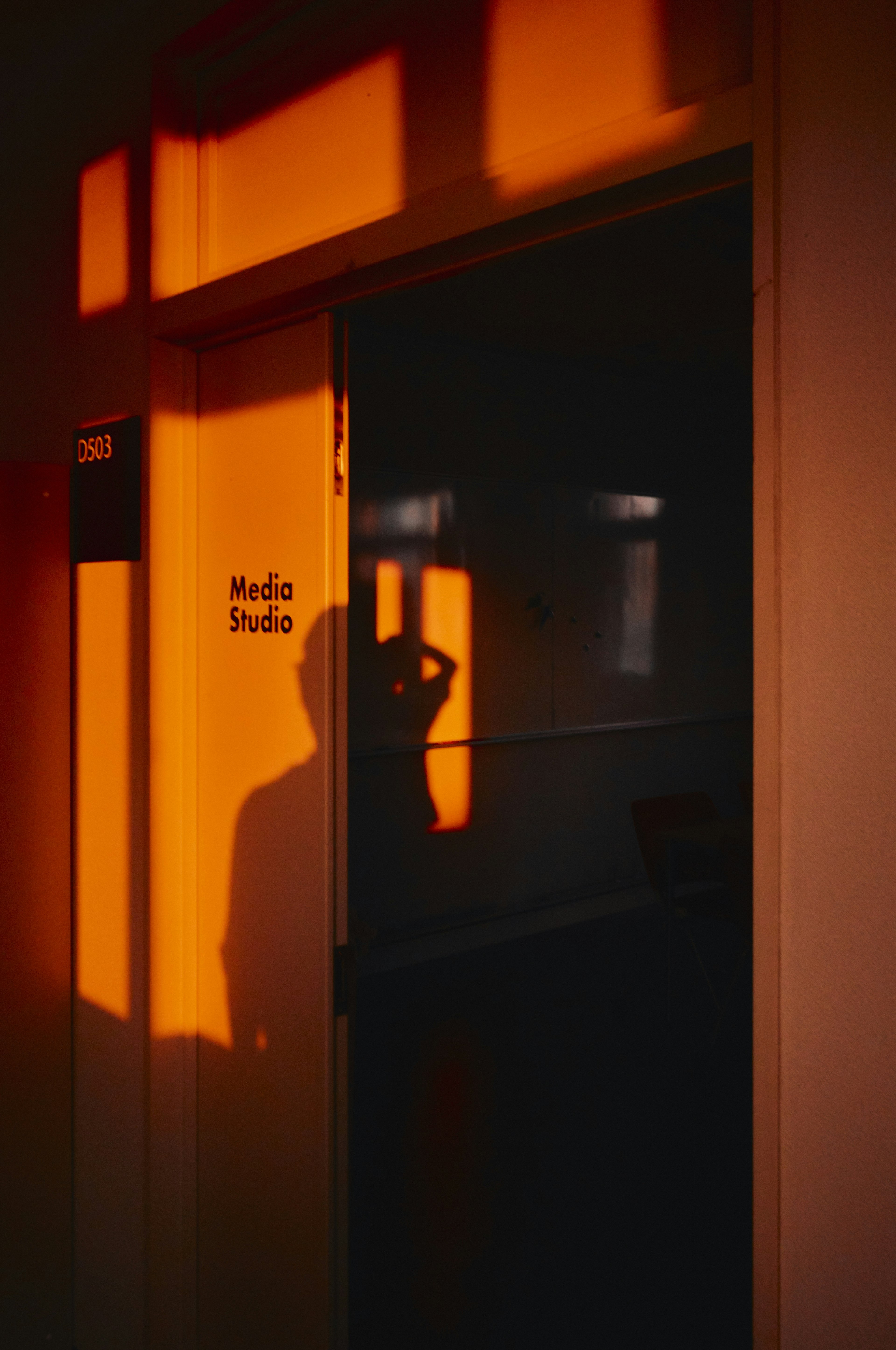 Silhouette di una persona davanti a una porta con ombre arancioni al tramonto