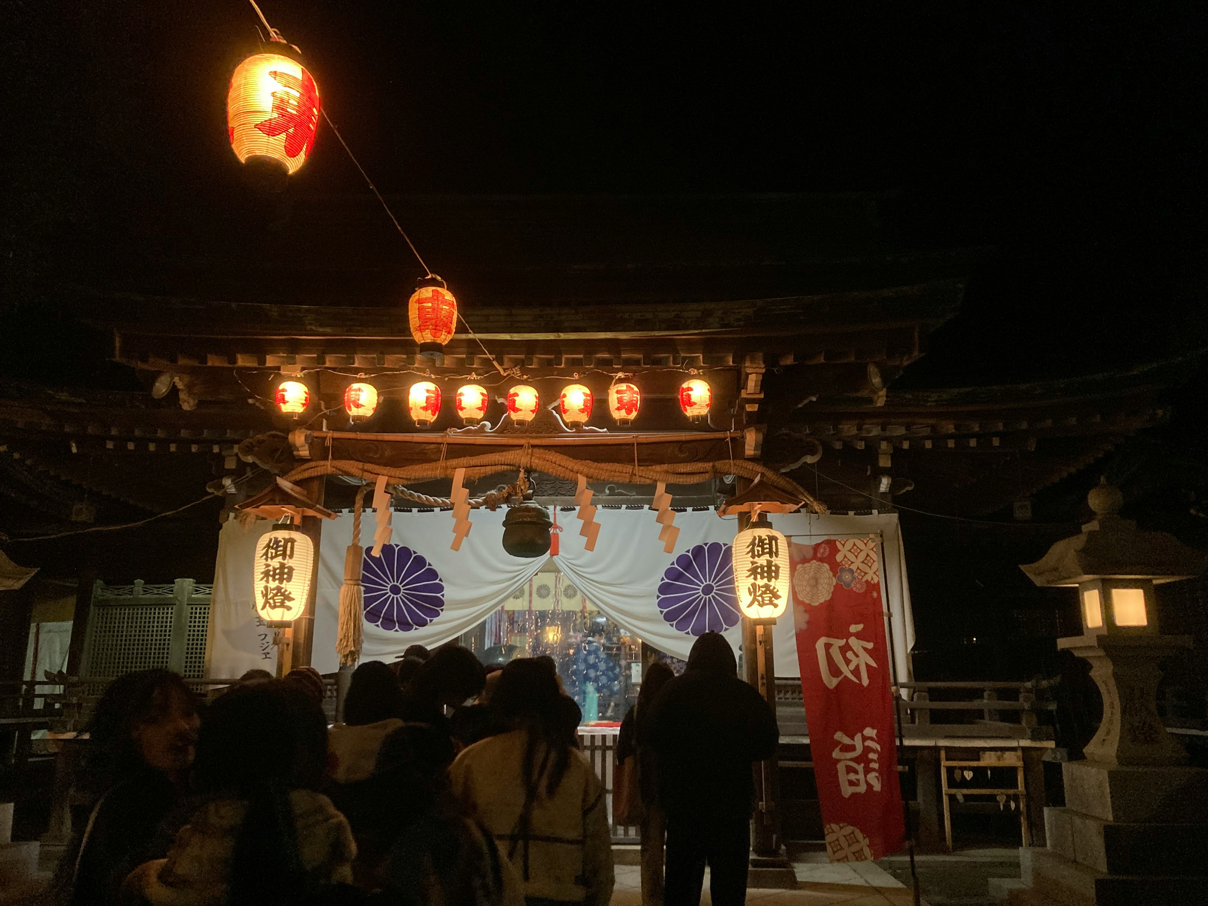 夜の神社の入り口に提灯が灯り人々が集まっている