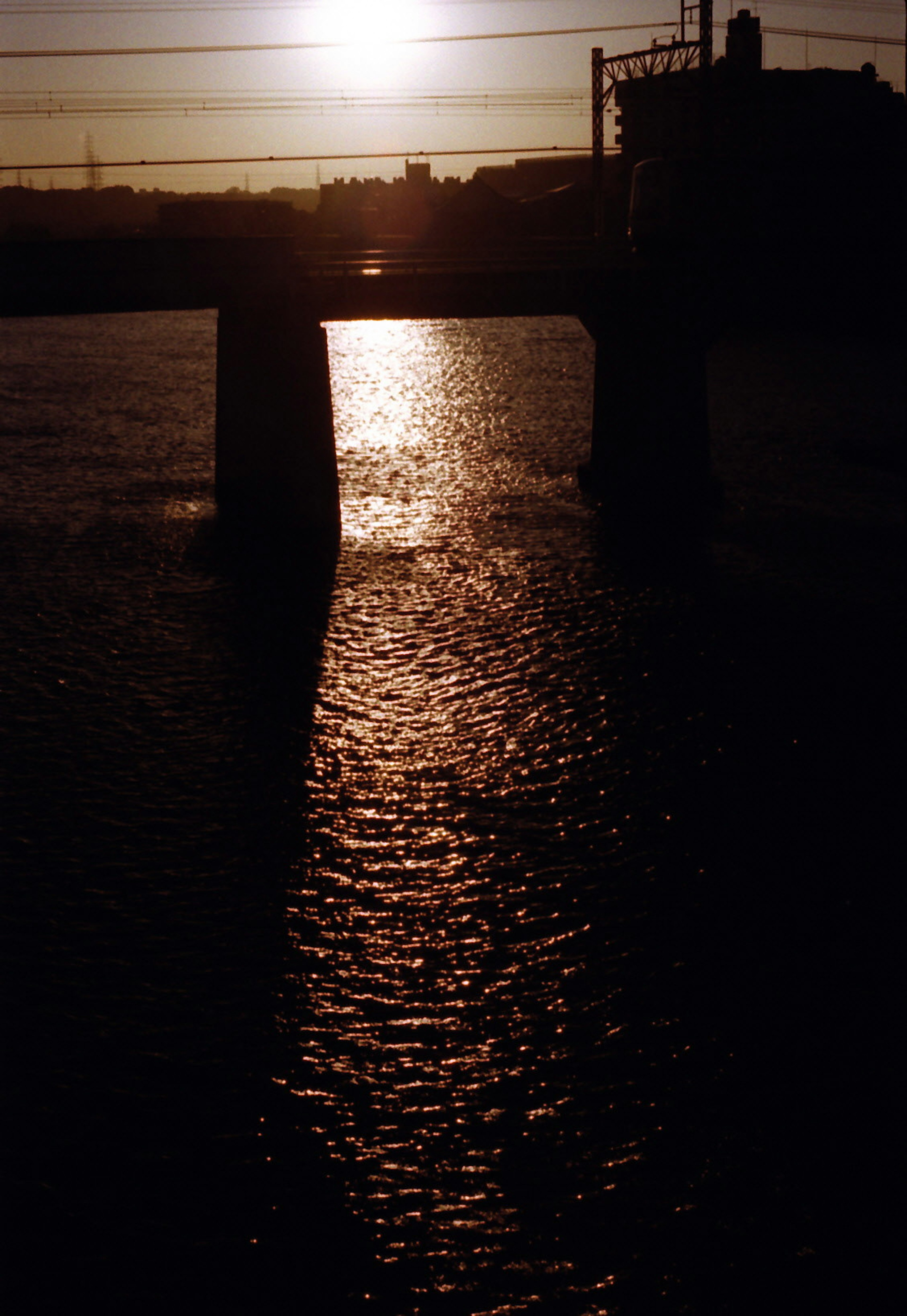 Silhouette jembatan dengan matahari terbenam yang memantul di permukaan air