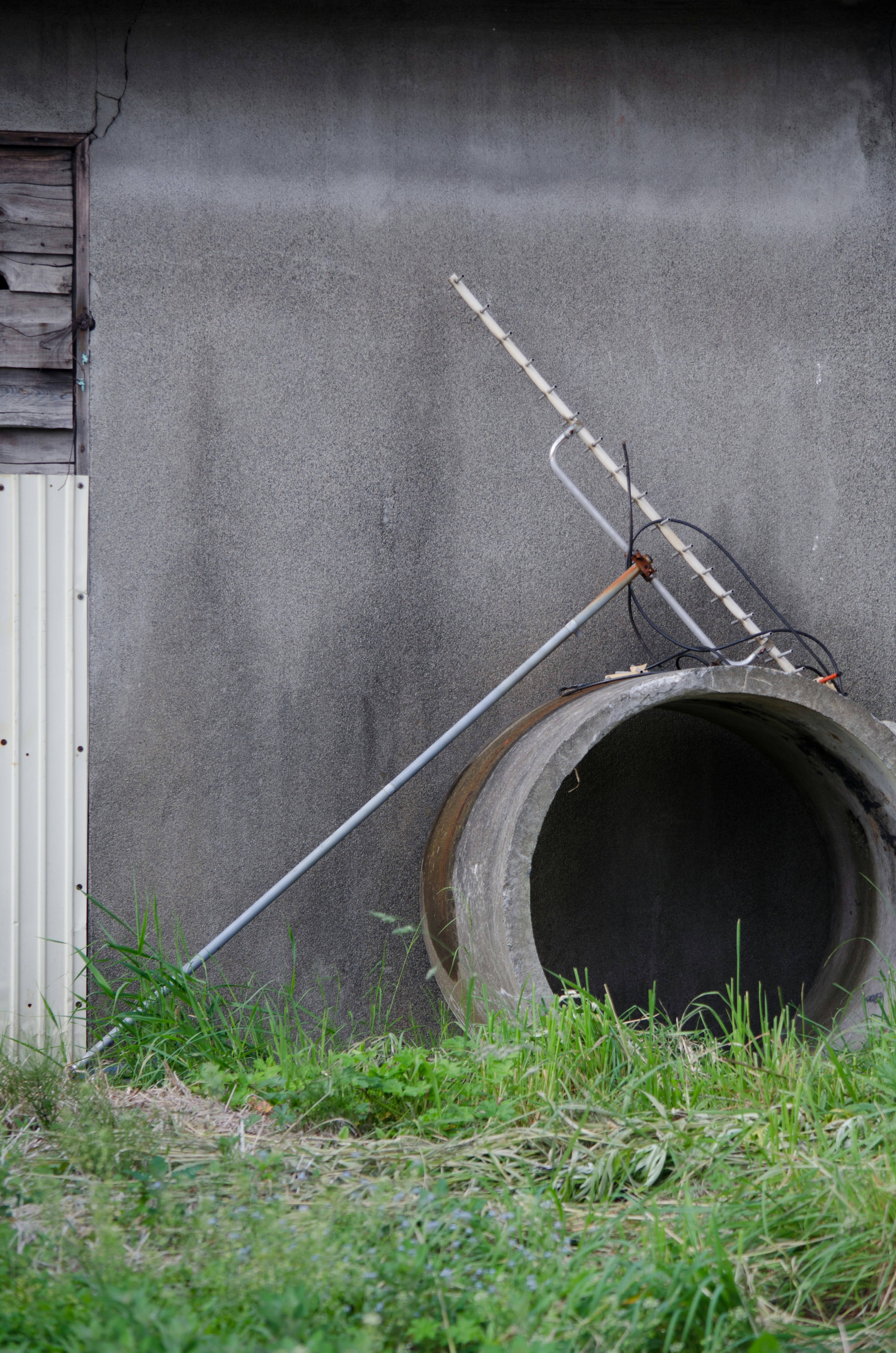 A metal tool leaning against a concrete pipe surrounded by grass