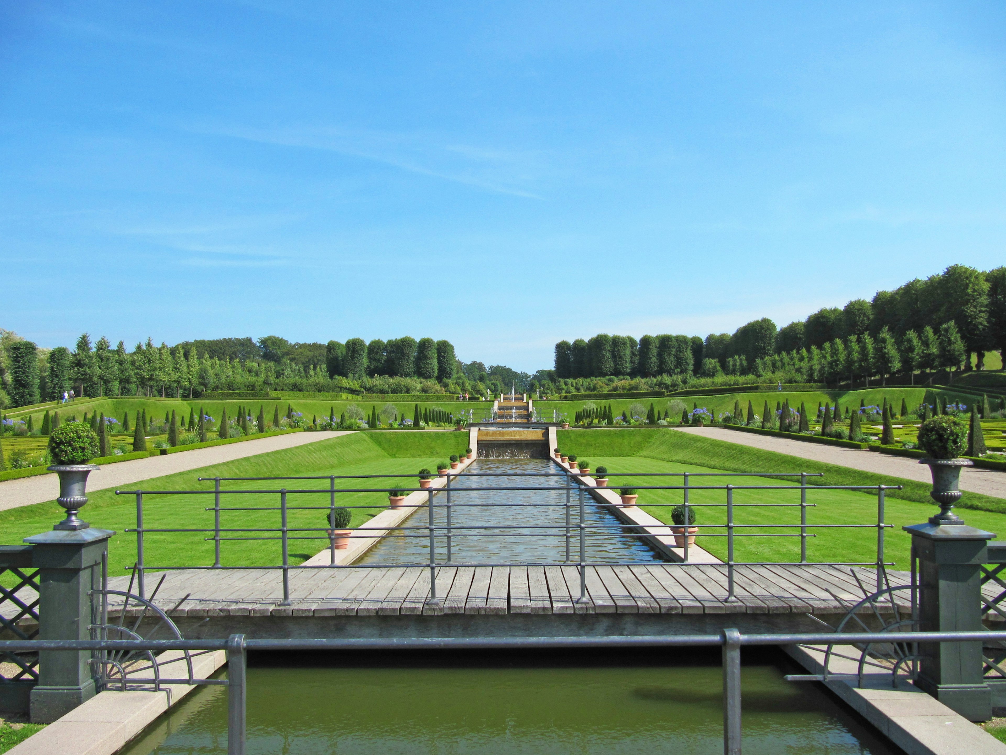 Vista di un bellissimo giardino con alberi verdi e prati curati Elemento d'acqua al centro che porta a gradini in lontananza