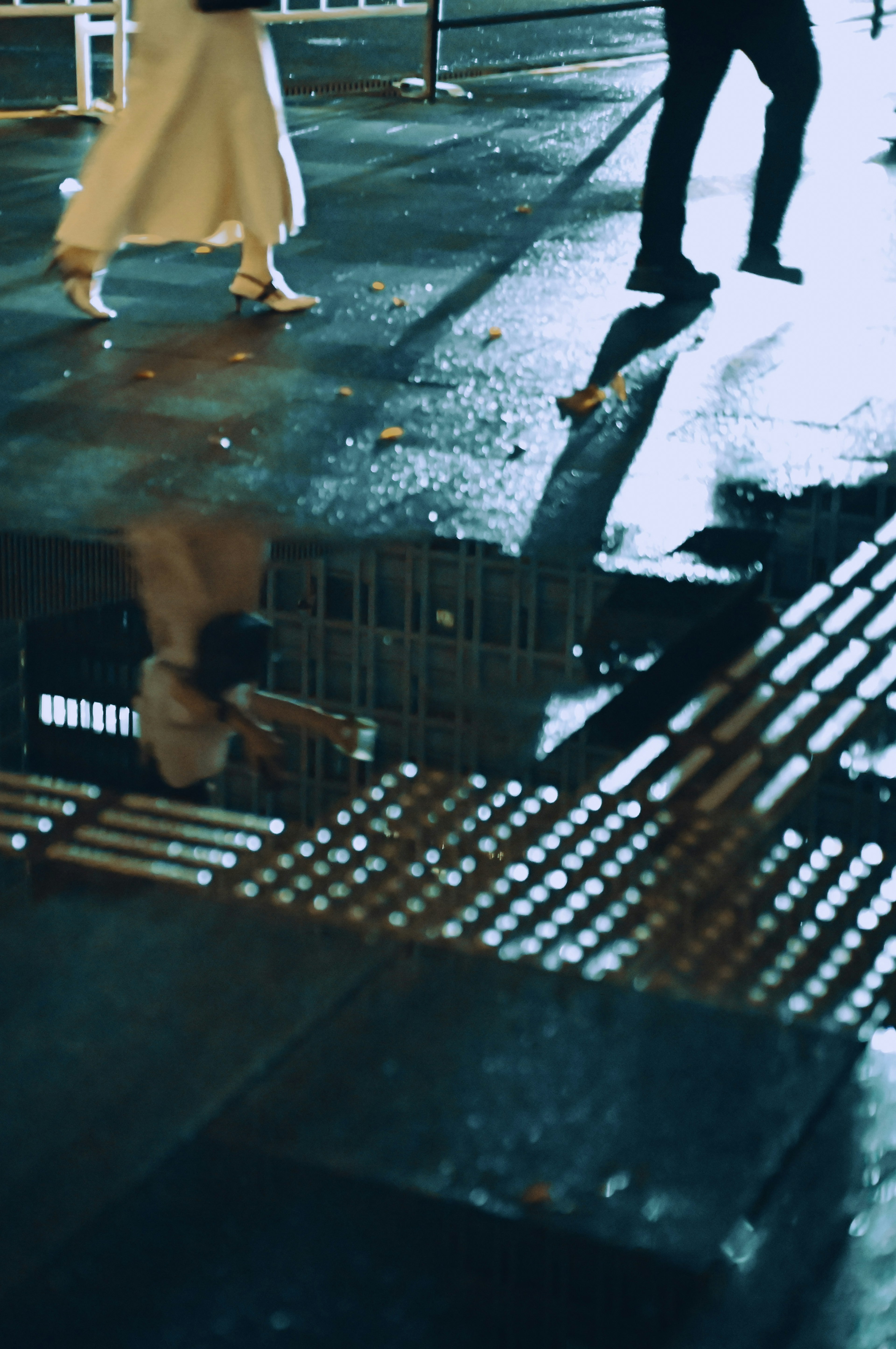 Silhouettes de personnes marchant sous la pluie reflétées dans une flaque