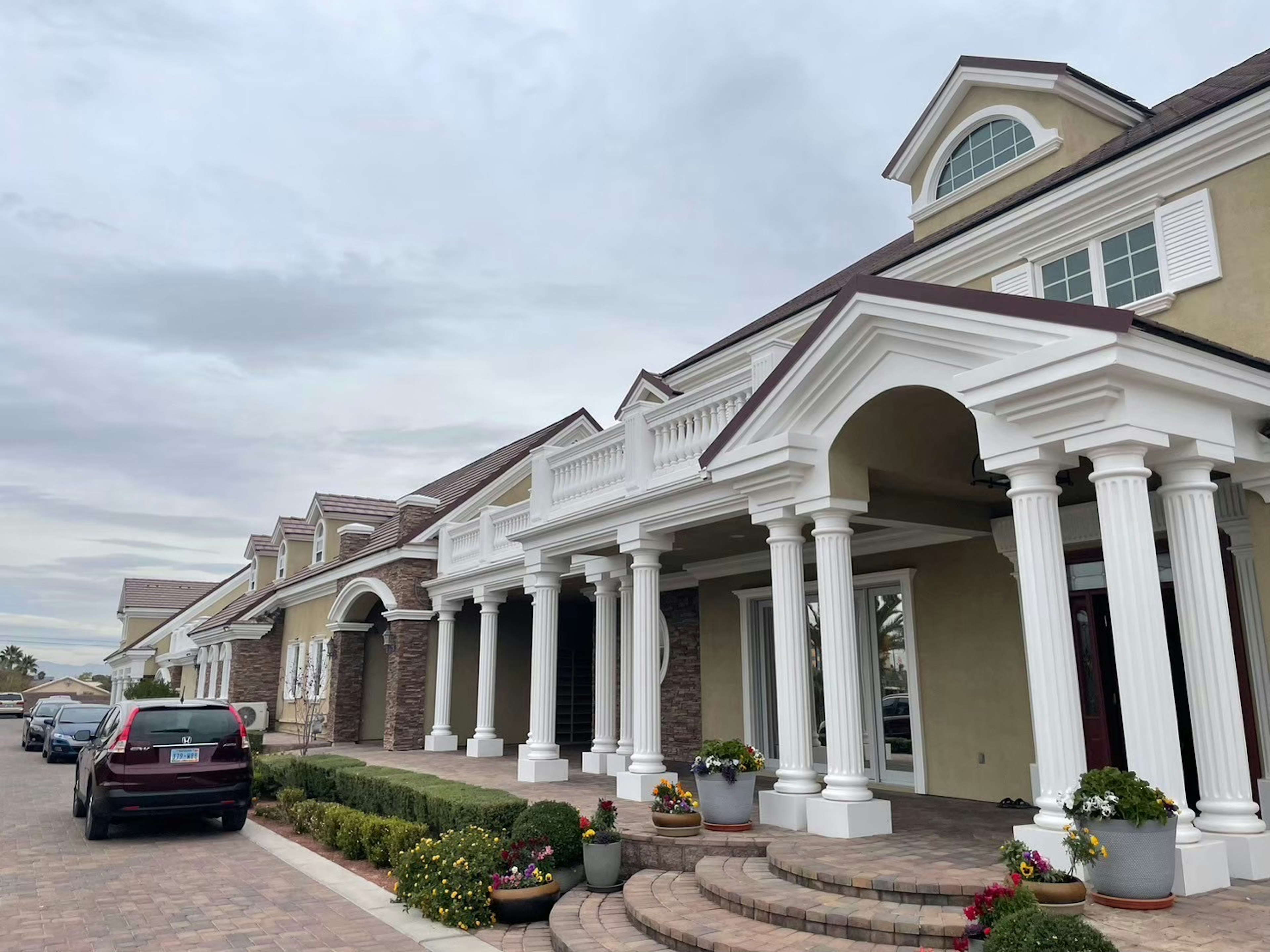 Elegant building exterior with white columns and greenery, parked car in the driveway