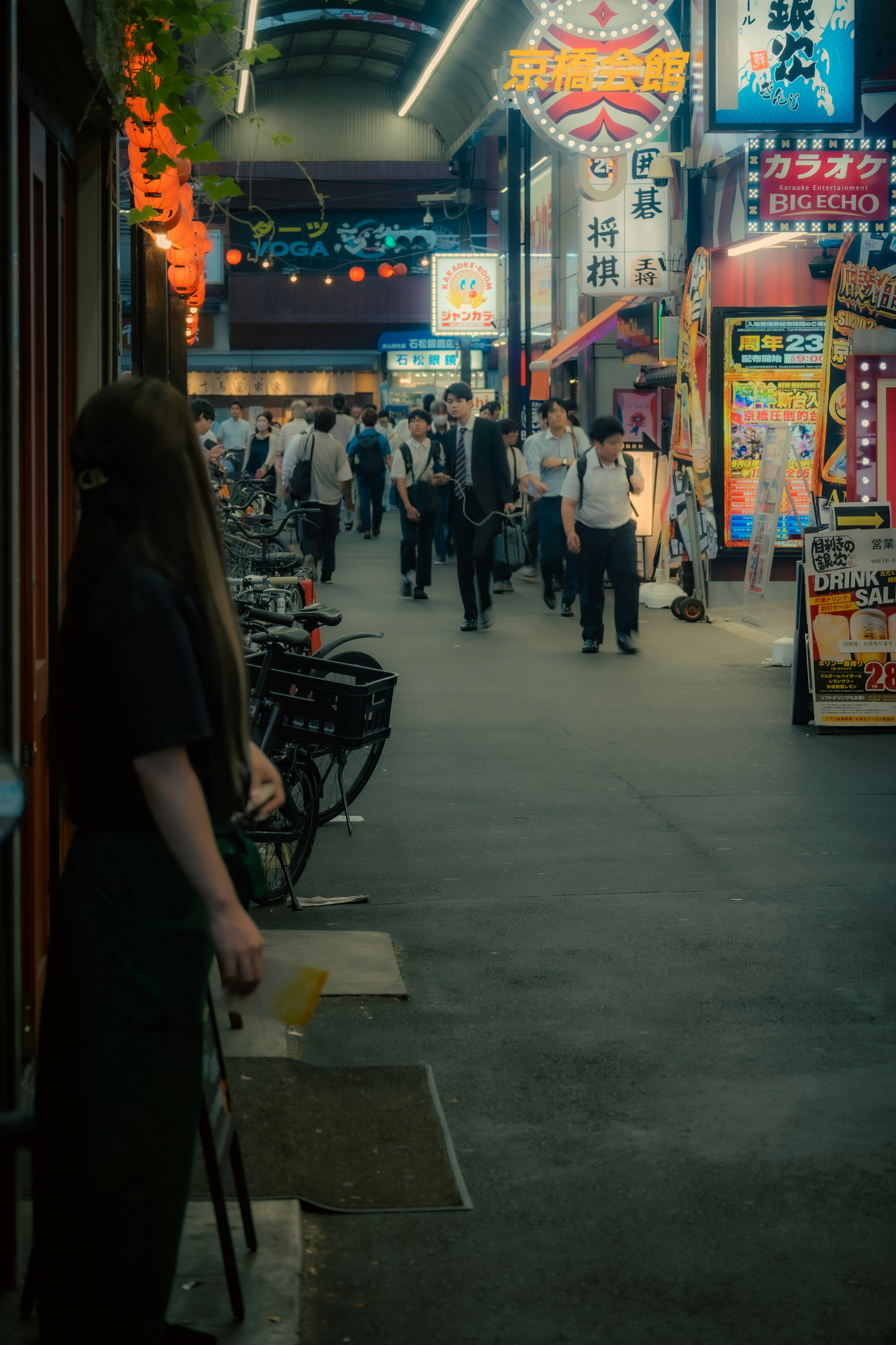 賑やかな商店街の通りで人々が歩いている様子が描かれています