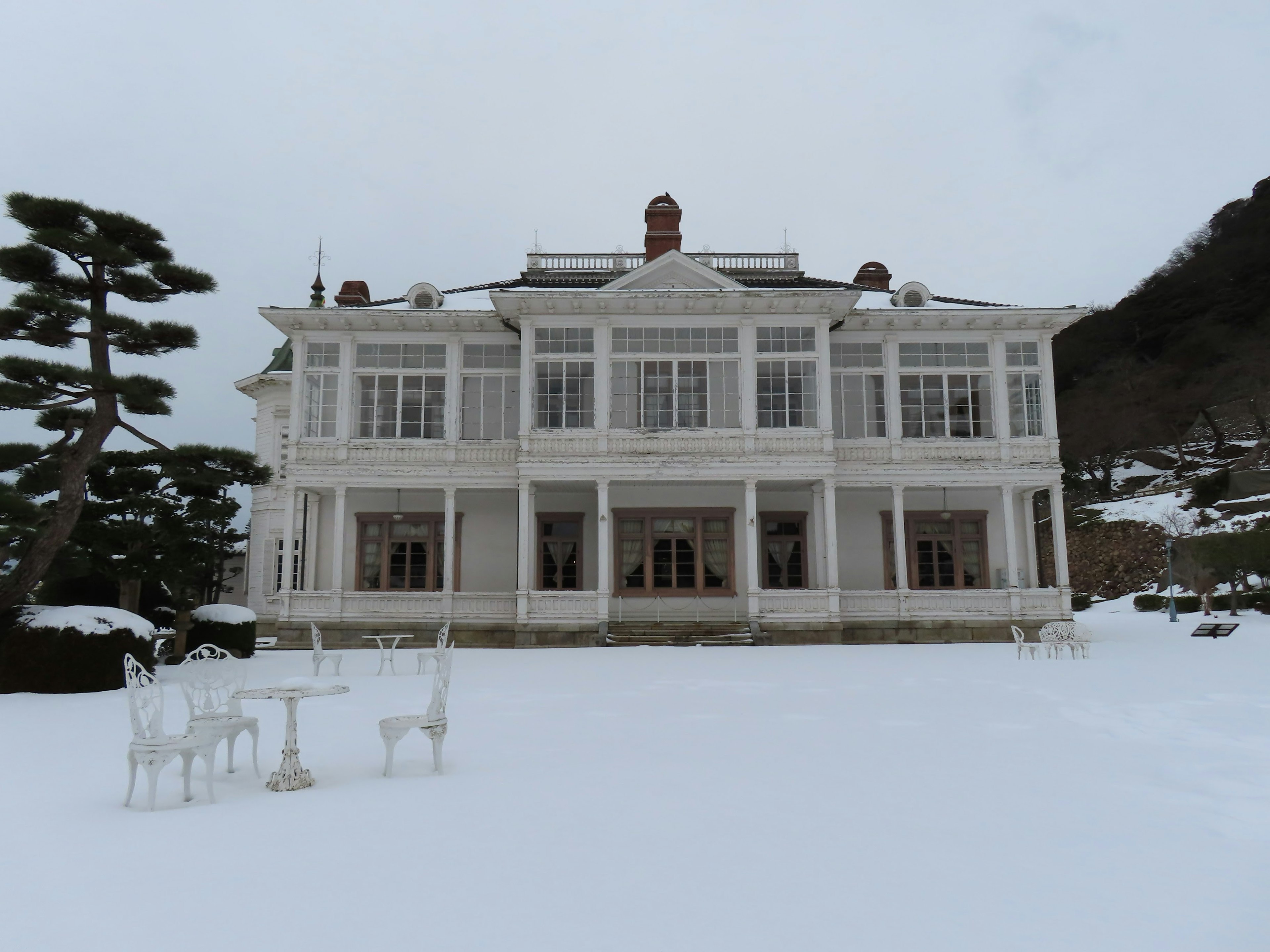 White mansion covered in snow with white table and chairs