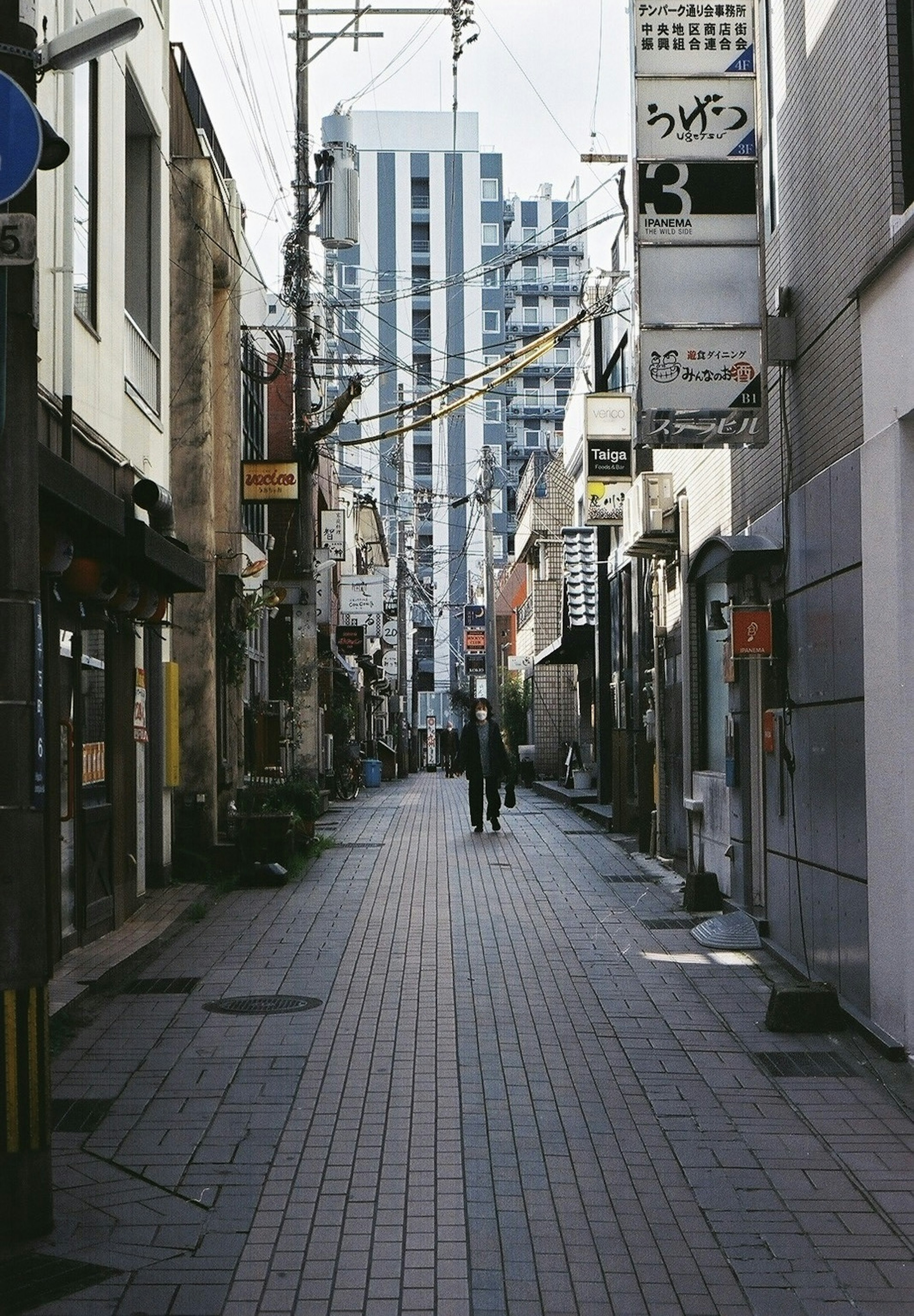 狭い路地に沿った商業ビルと住宅が立ち並ぶ風景