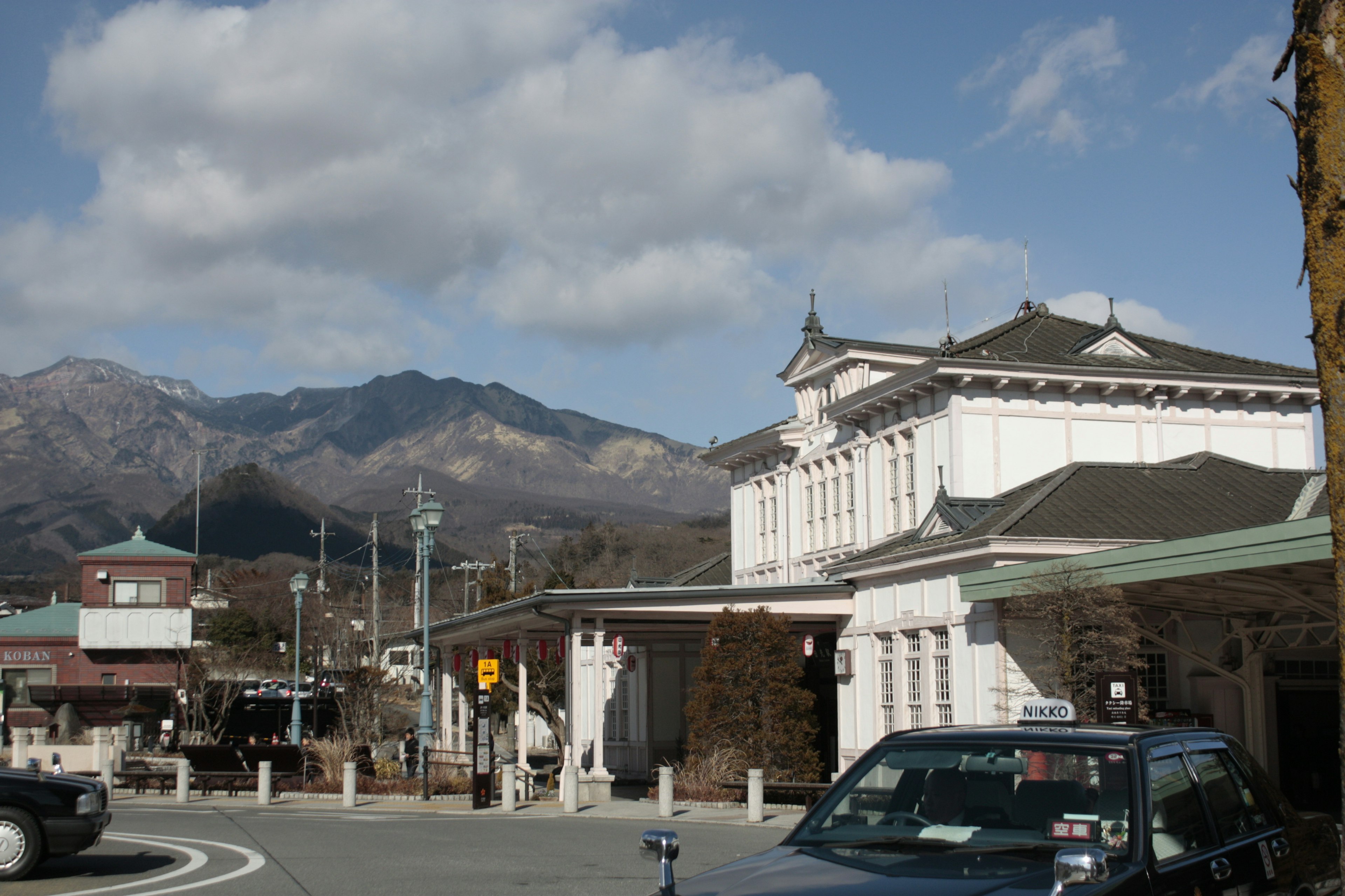 山々を背景にした古い駅舎と車両が見える風景