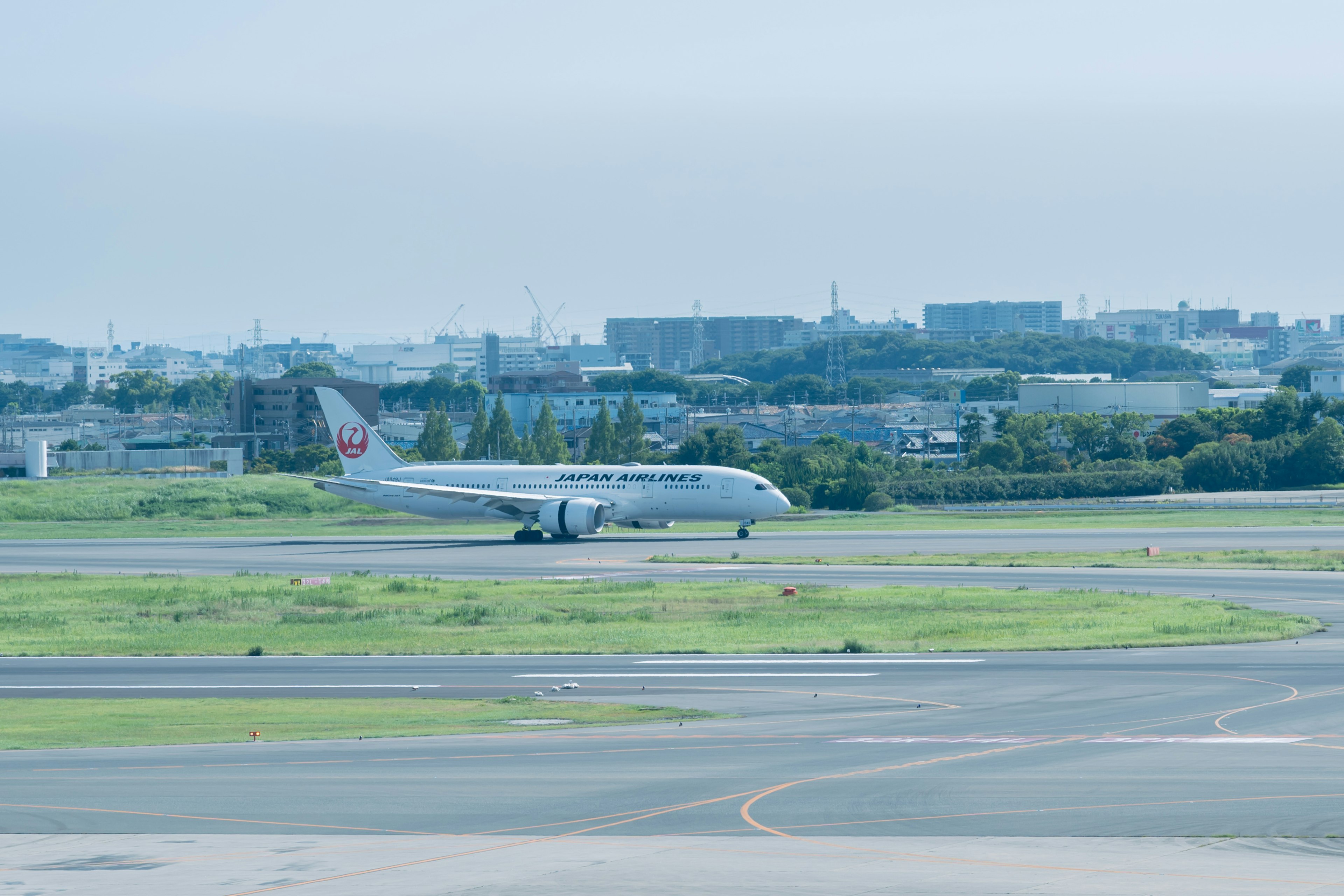 เครื่องบิน Japan Airlines ที่กำลังเคลื่อนตัวบนรันเวย์สนามบินพร้อมทิวทัศน์เมืองด้านหลัง