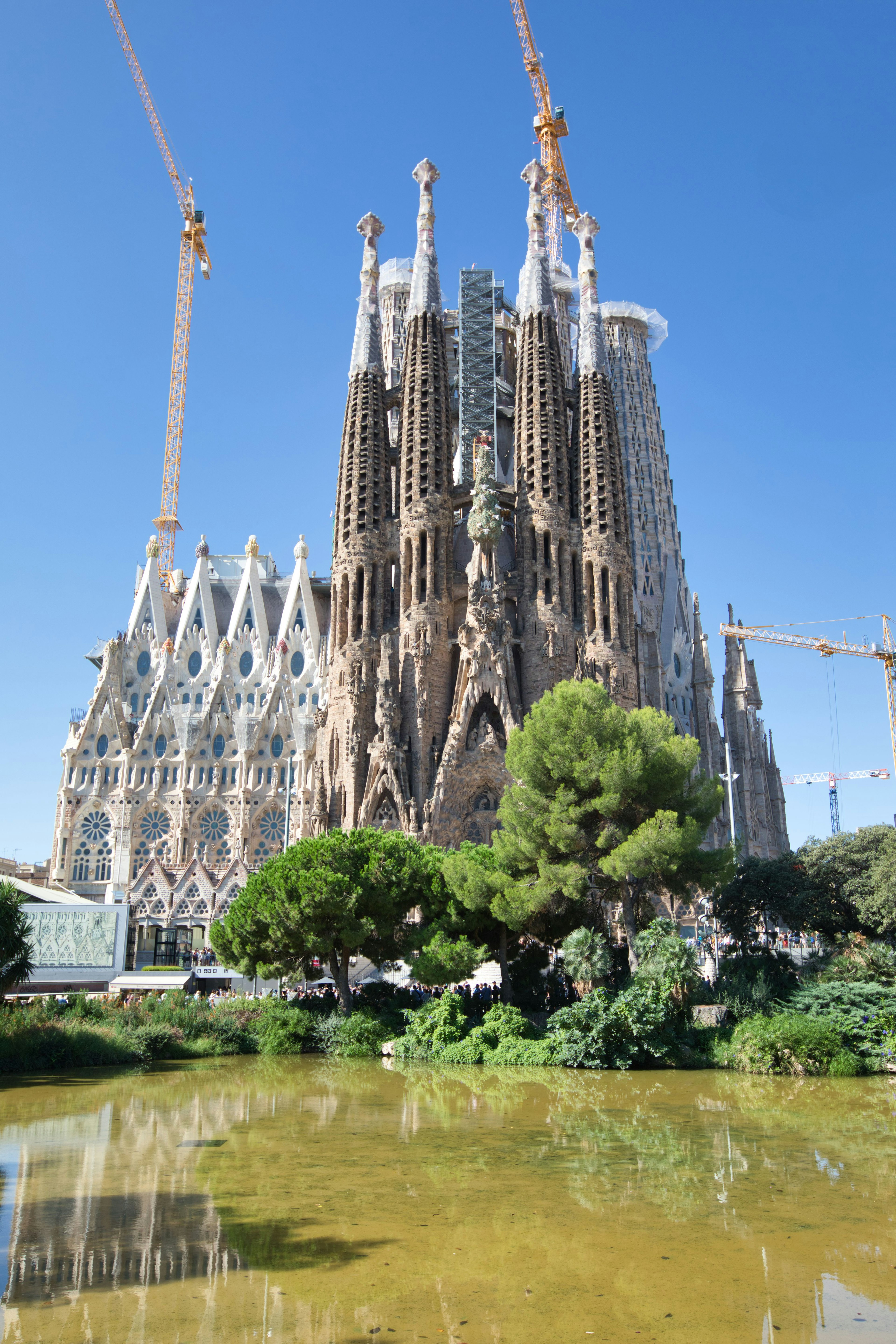 Under construction Sagrada Familia with green foliage and pond