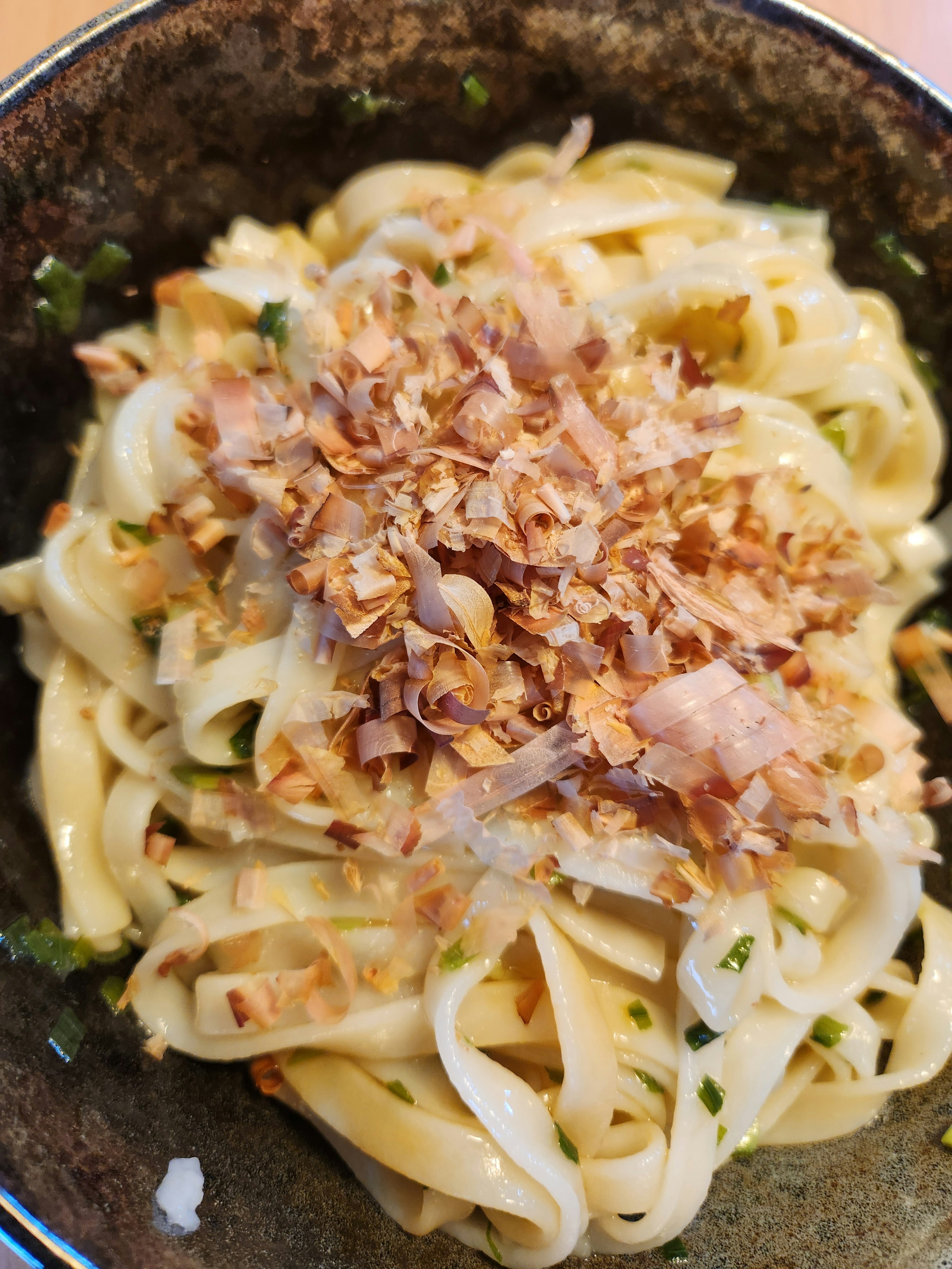 Thick noodles coated in creamy sauce topped with crunchy flakes