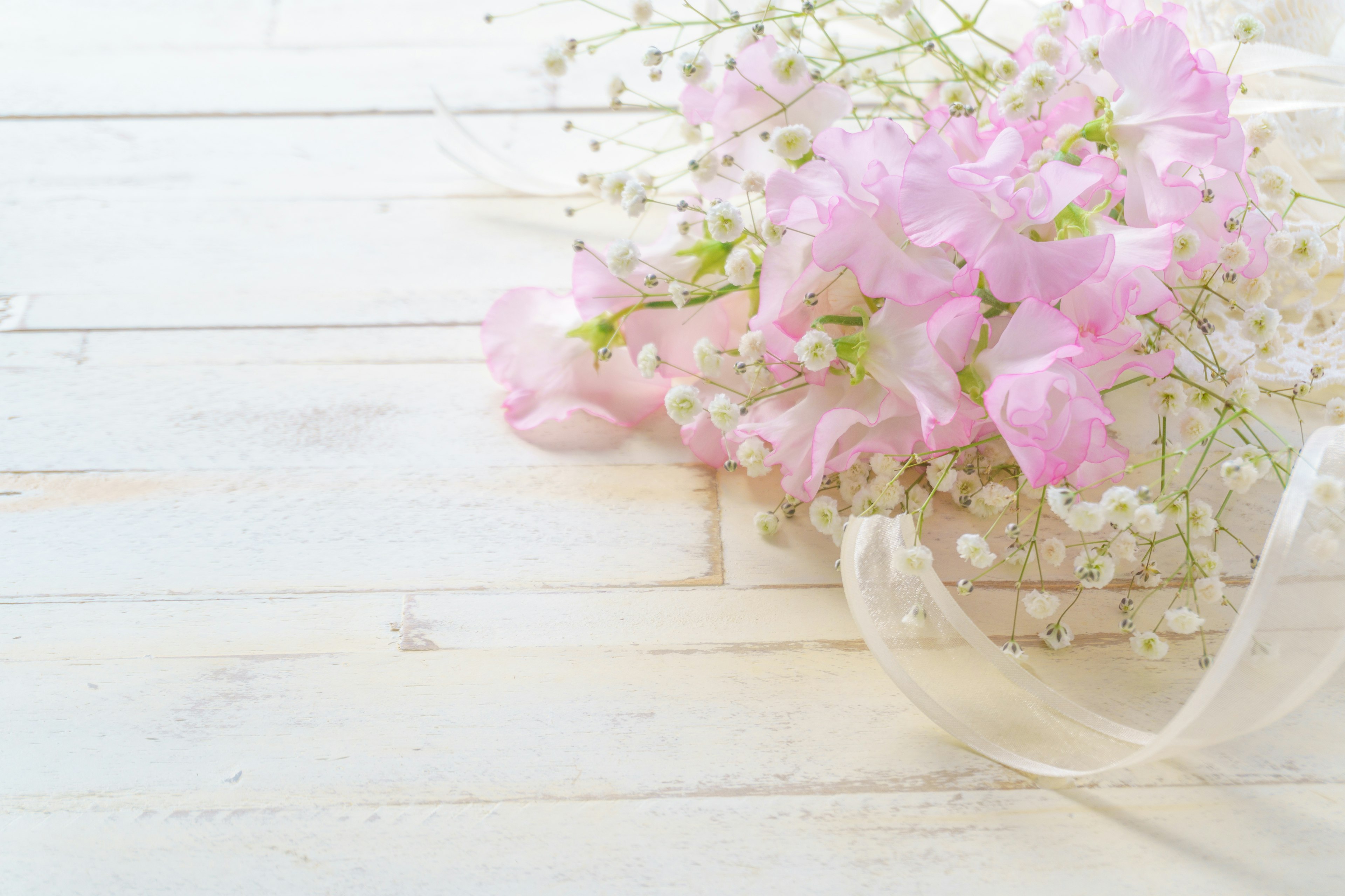 Delicate pink flowers and baby breath arranged on a white wooden table