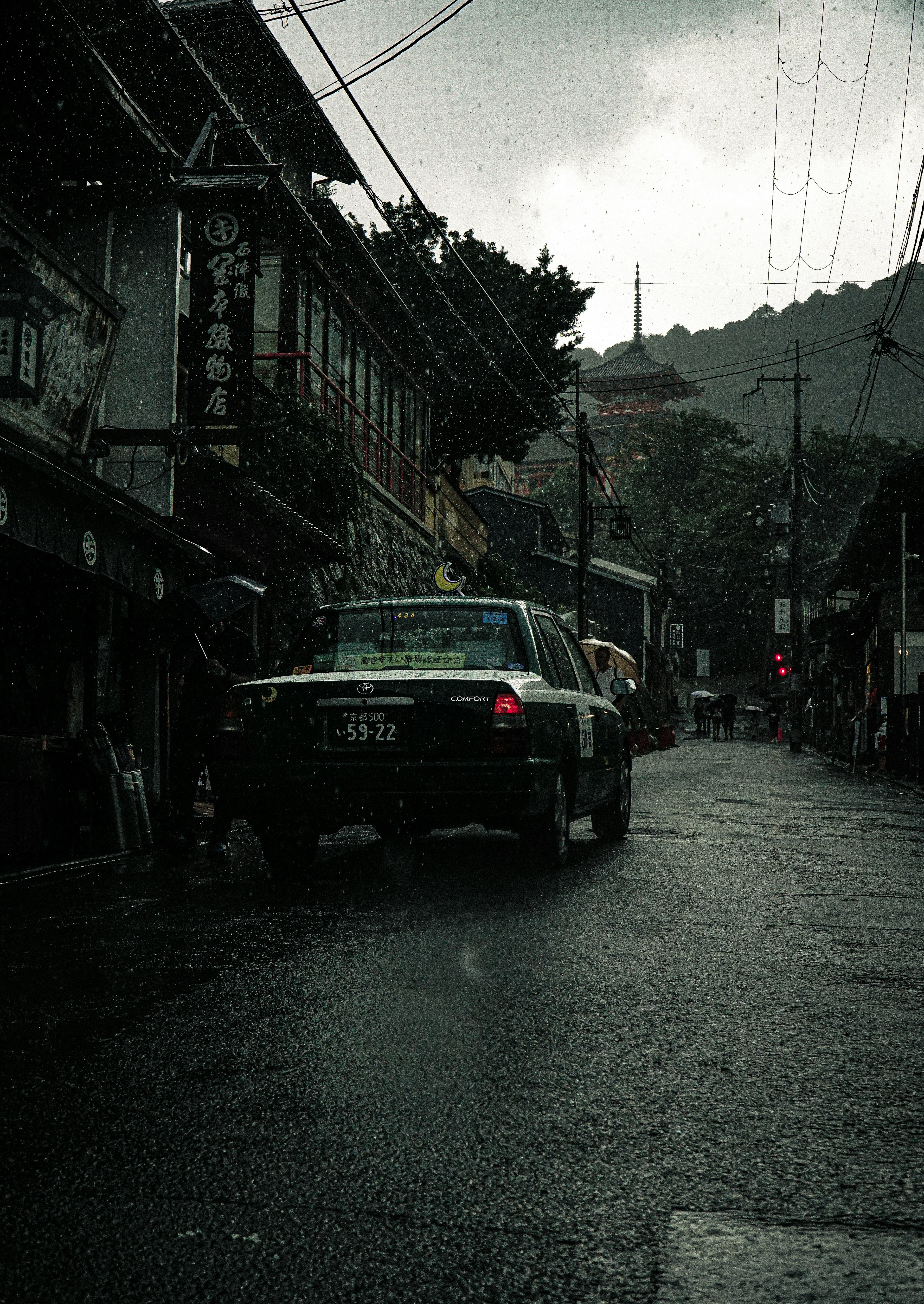 雨の降る街並みと古い建物が見える狭い通りに停まった車