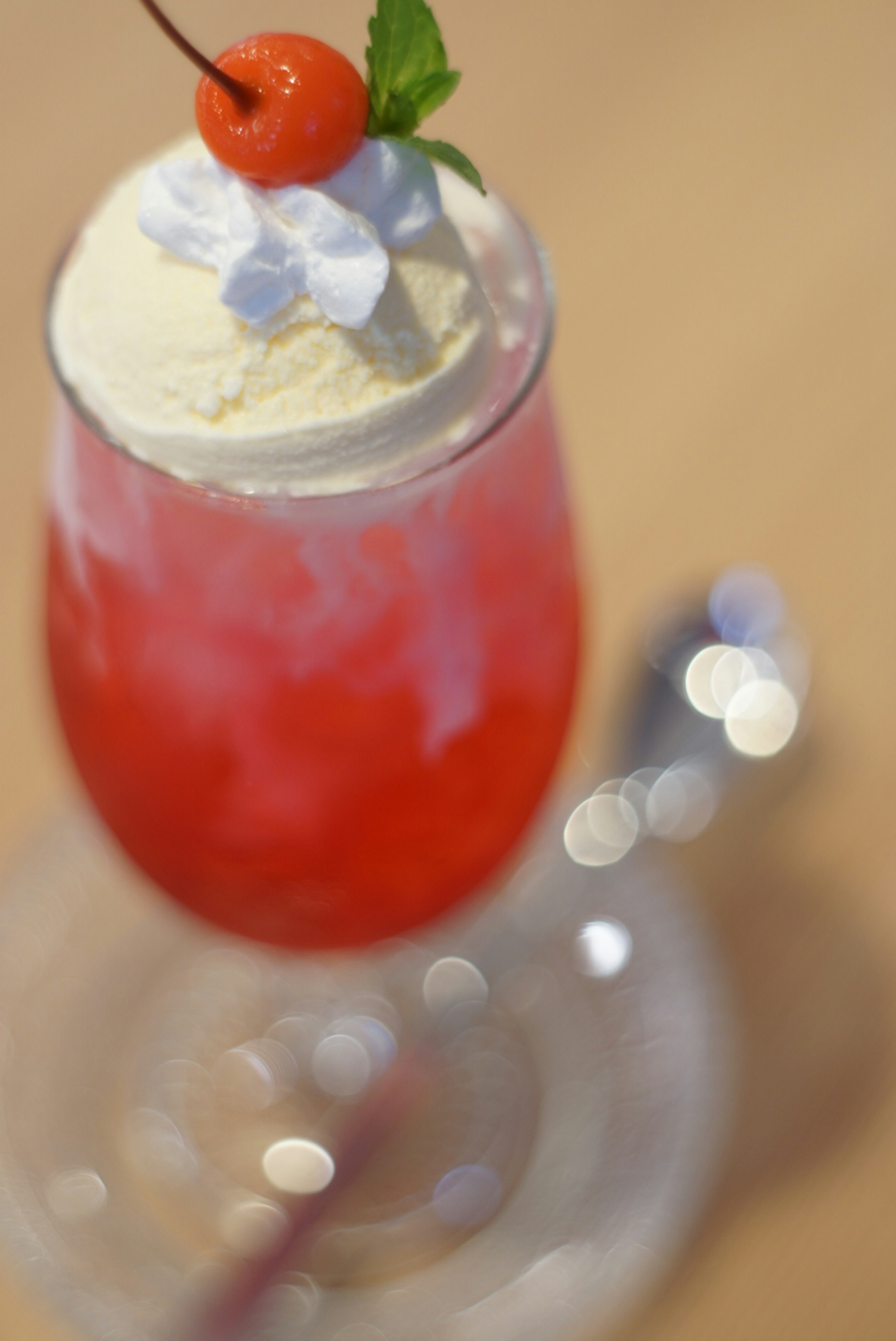 A glass of red beverage topped with whipped cream and a cherry