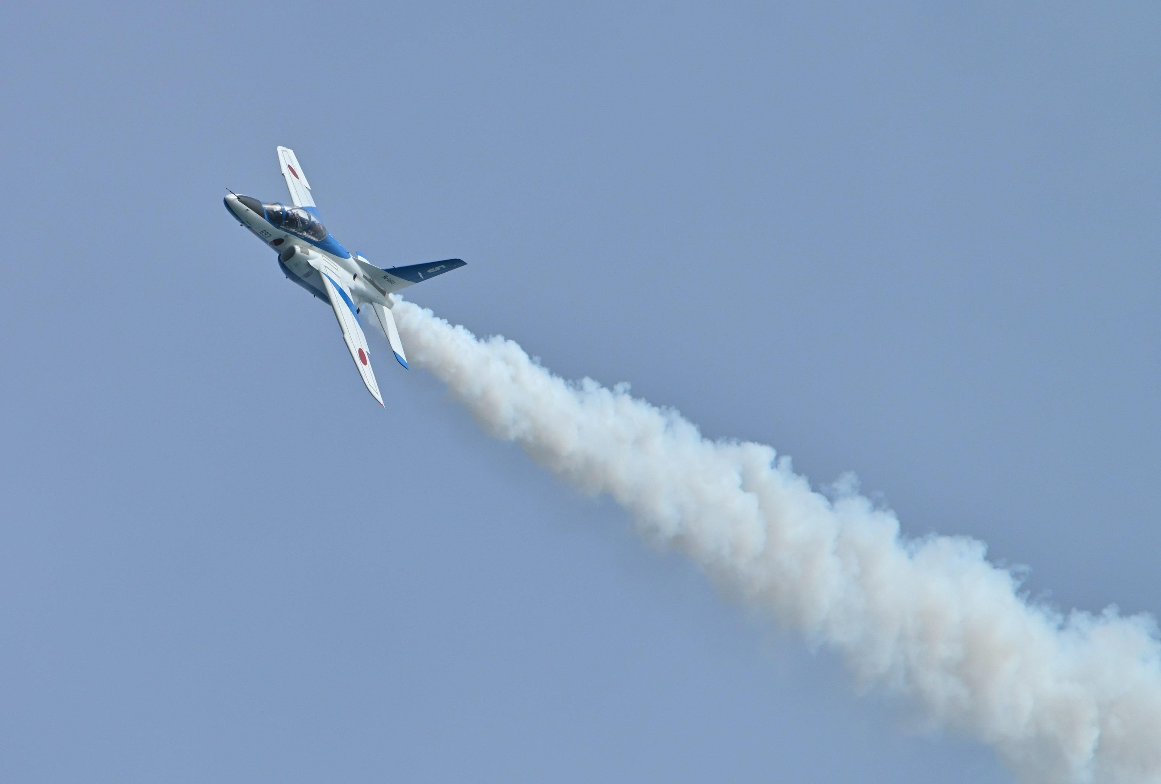 Un aereo che vola contro un cielo blu lasciando una scia di fumo