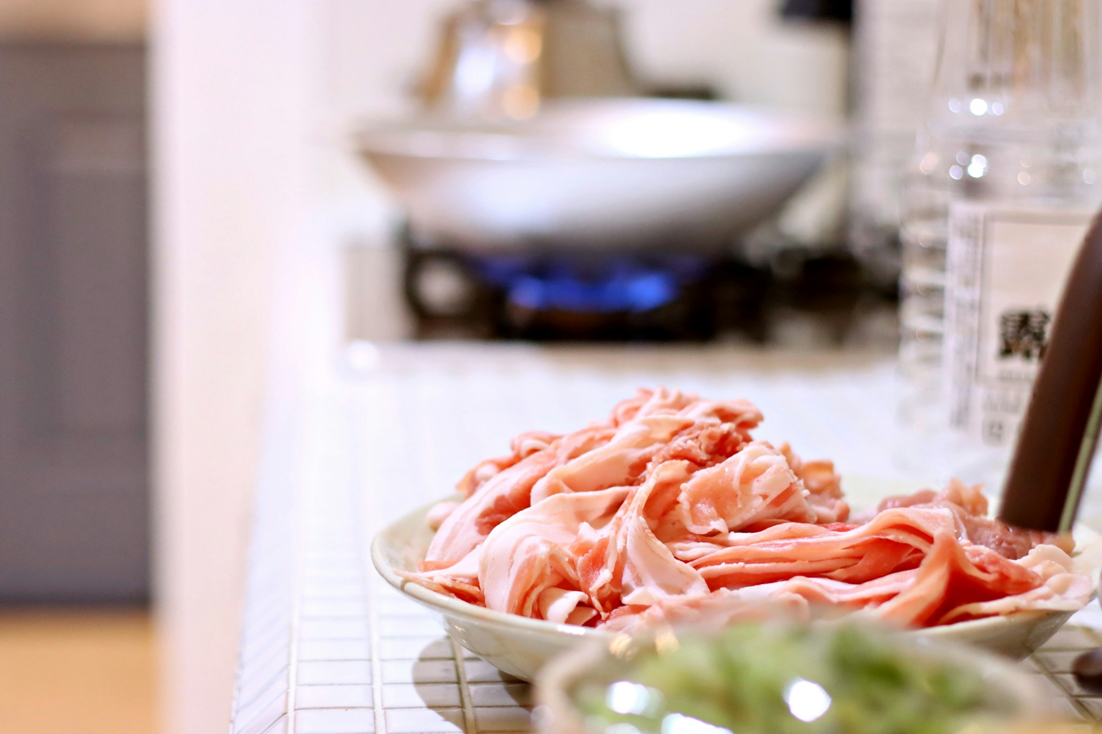 Une scène de cuisine avec du porc tranché finement sur une assiette et une cuisinière en arrière-plan