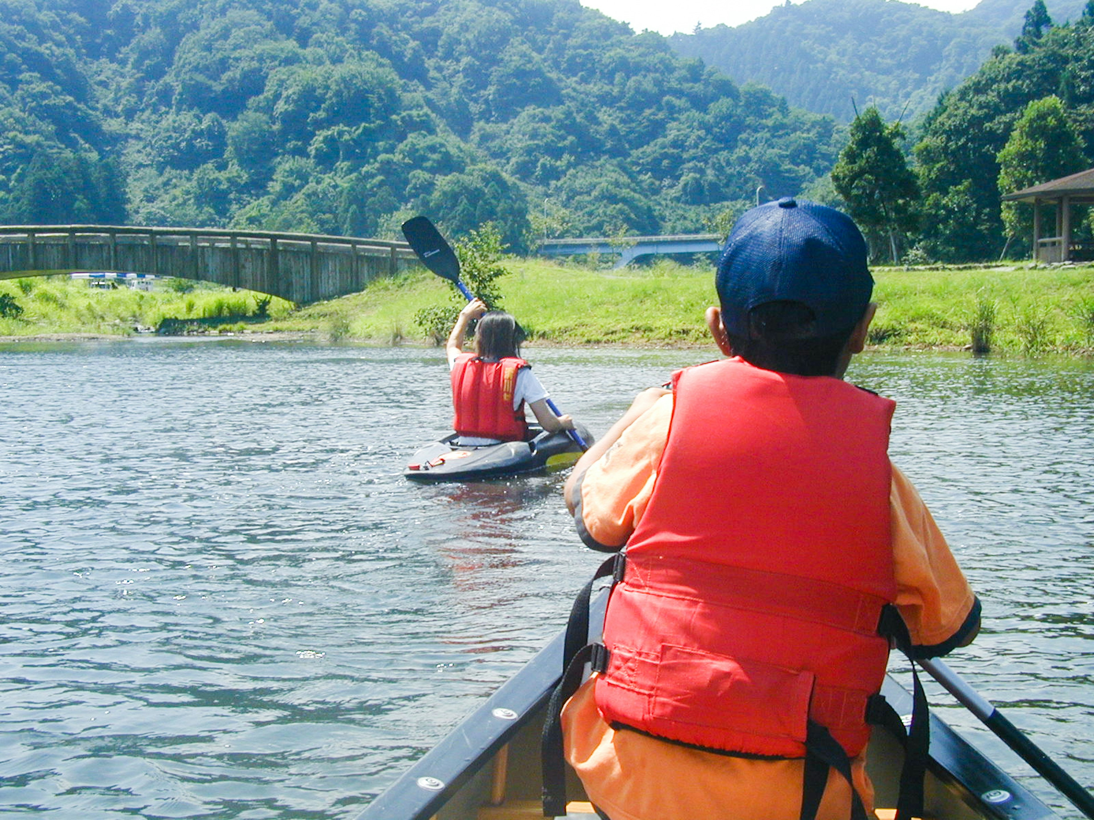 川でカヤックを漕ぐ子供たちと緑の山の風景