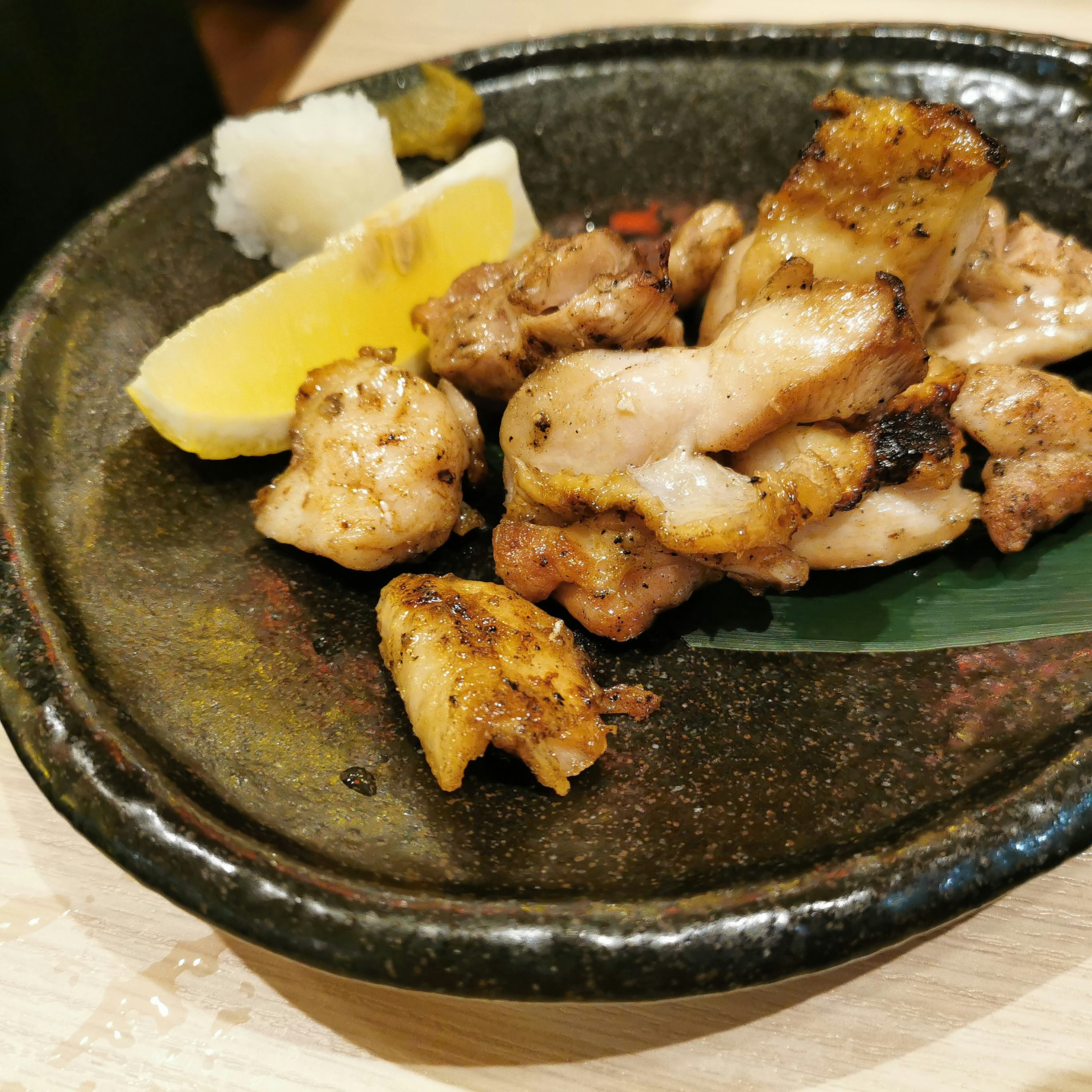 Morces de poulet grillé servis sur une assiette noire avec des tranches de citron