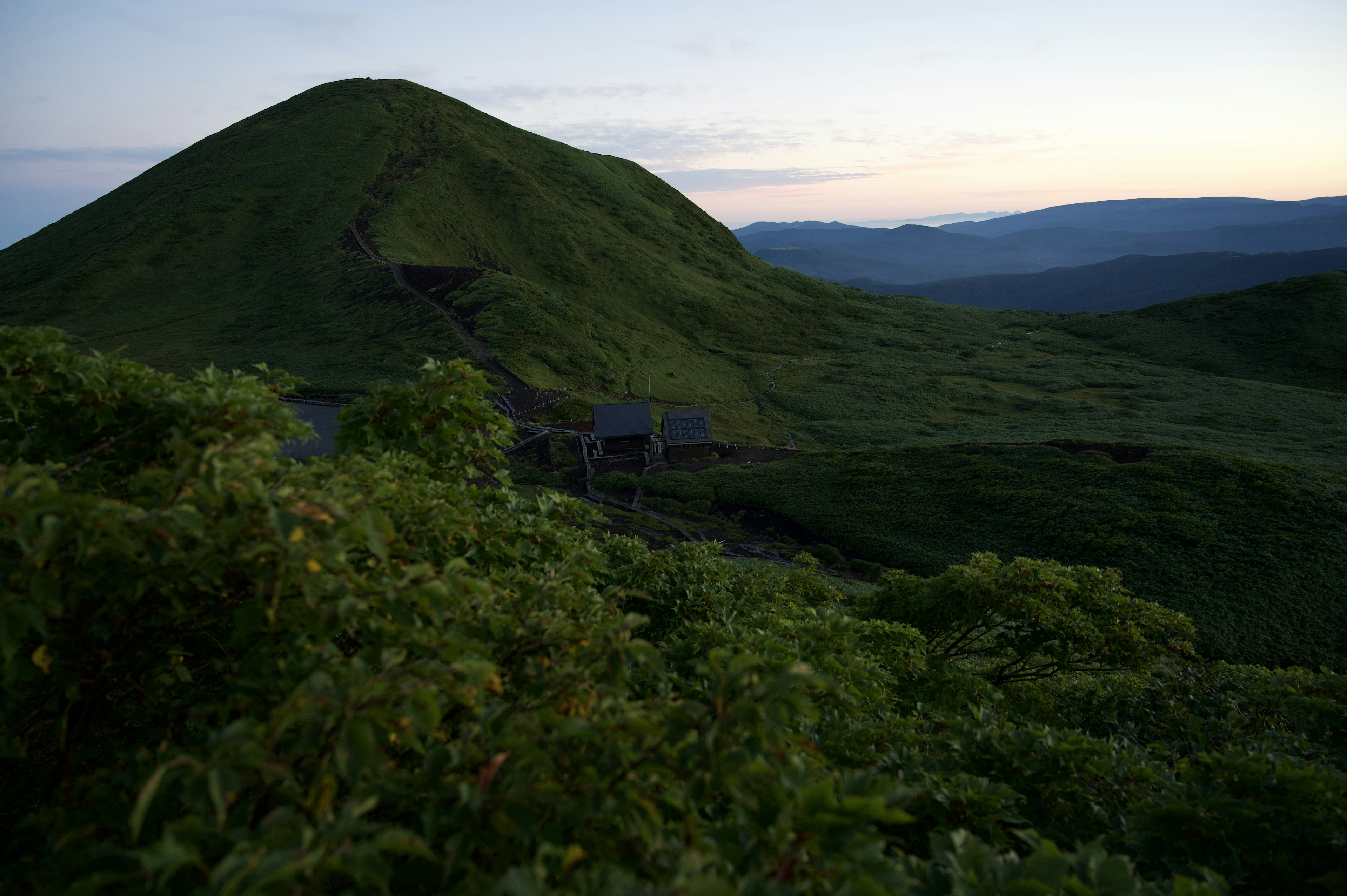 Un paesaggio con colline verdi e montagne lontane al crepuscolo