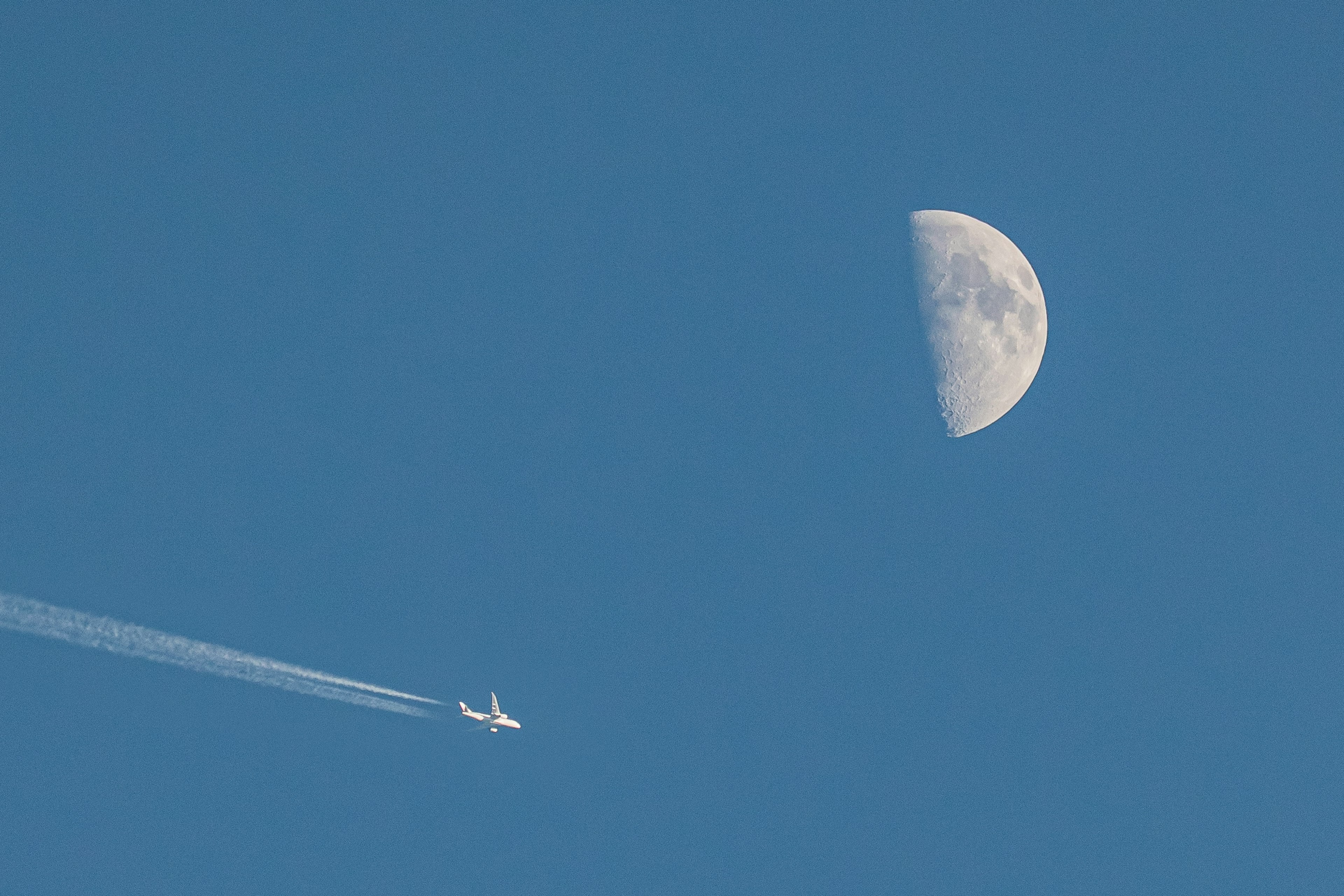 Una media luna en el cielo azul con un avión dejando una estela