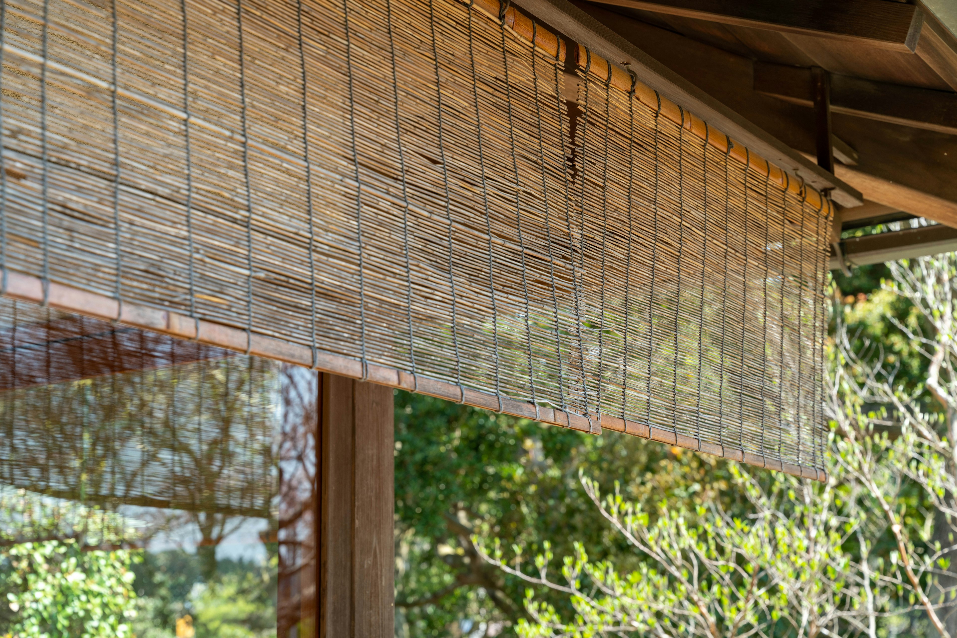 Écran en bambou suspendu sous un toit en bois avec une verdure naturelle en arrière-plan