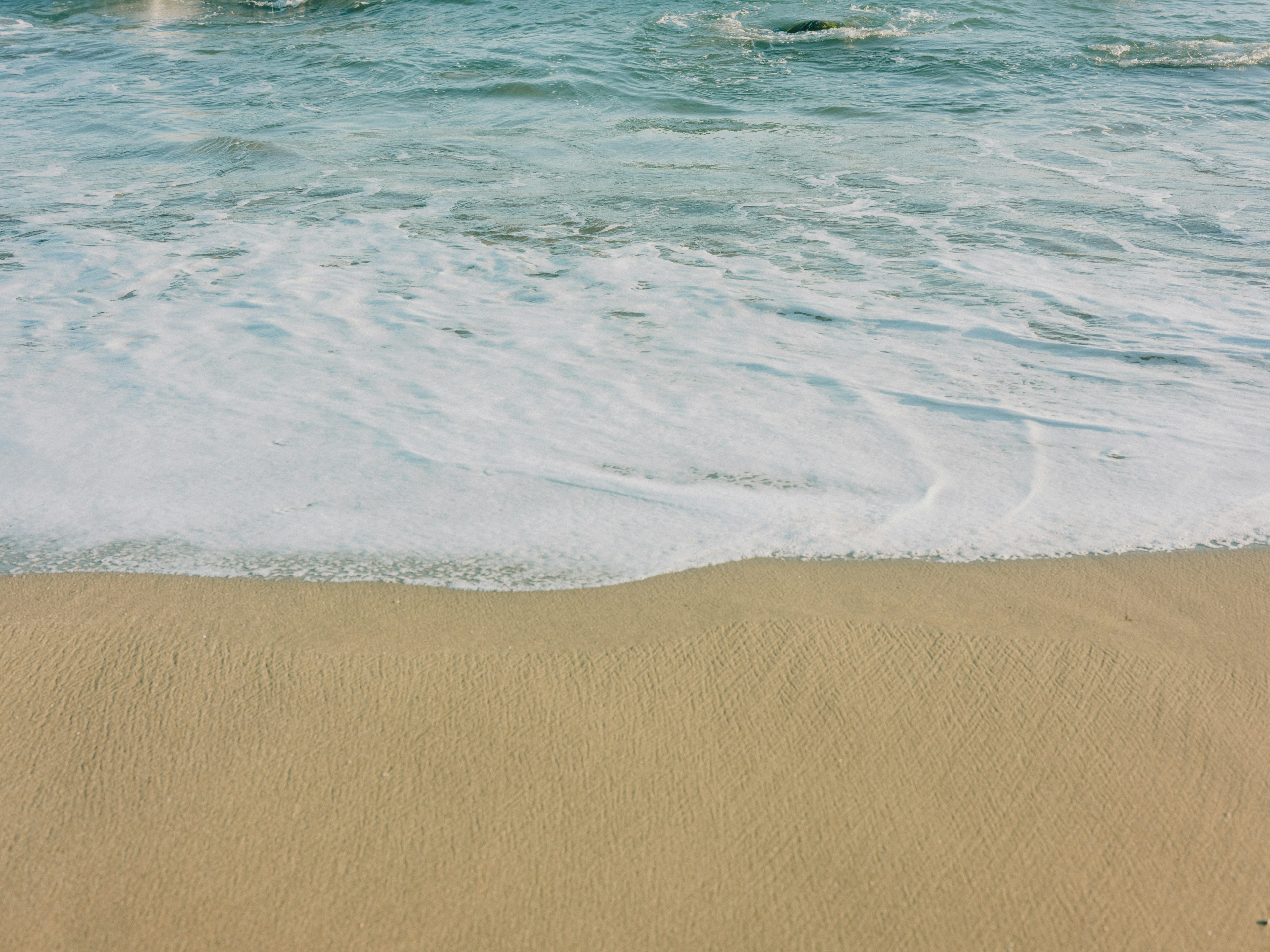 คลื่นทะเลสีน้ำเงินกระทบชายหาดทรายอย่างอ่อนโยน