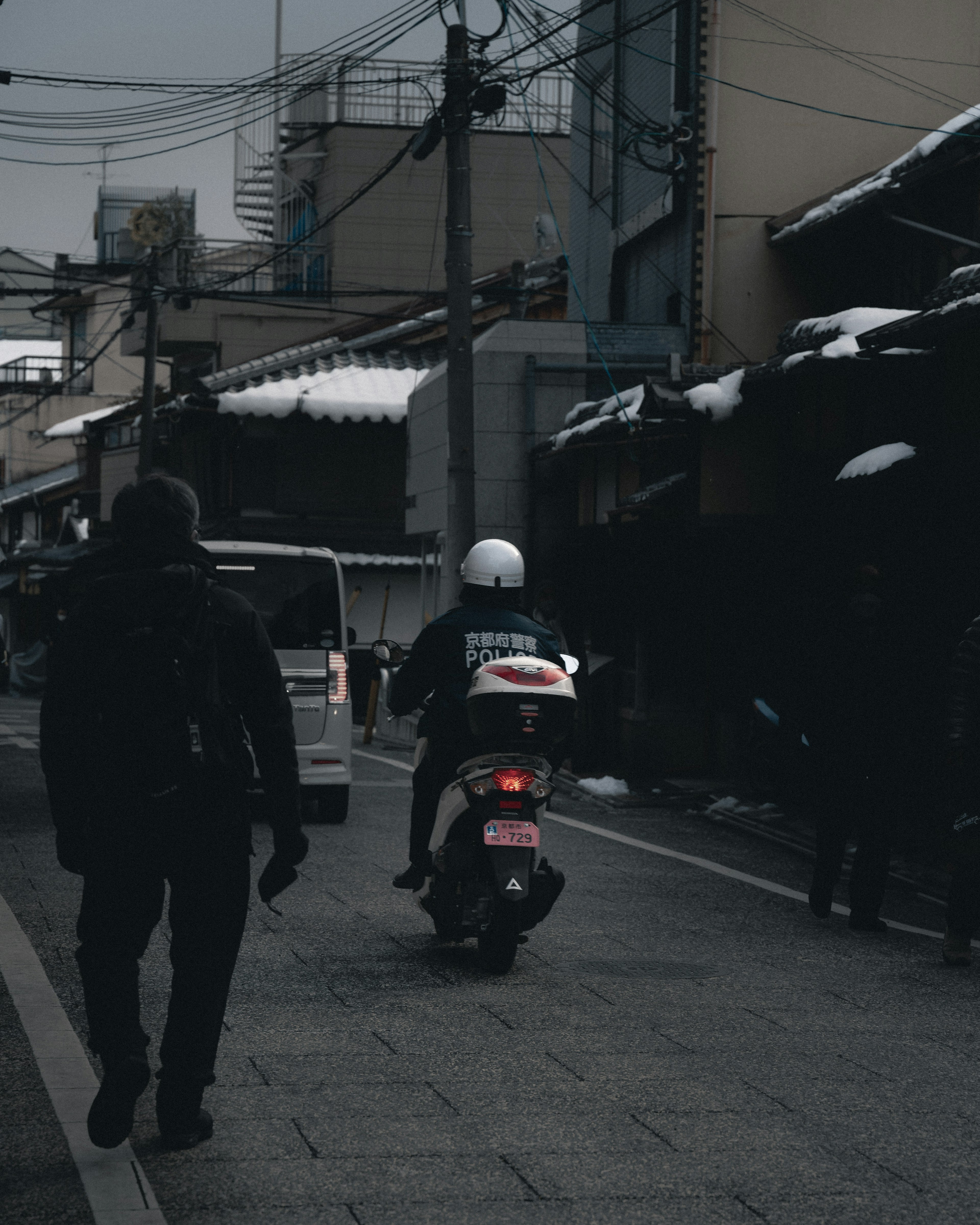 A person walking in a snowy urban street with a delivery scooter