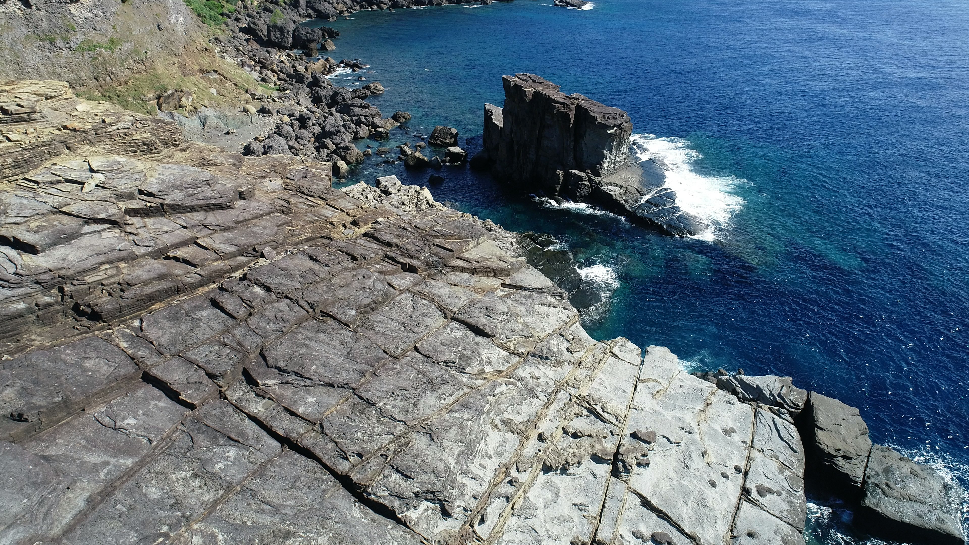 海に面した岩場の風景で、青い海と岩の層が見える